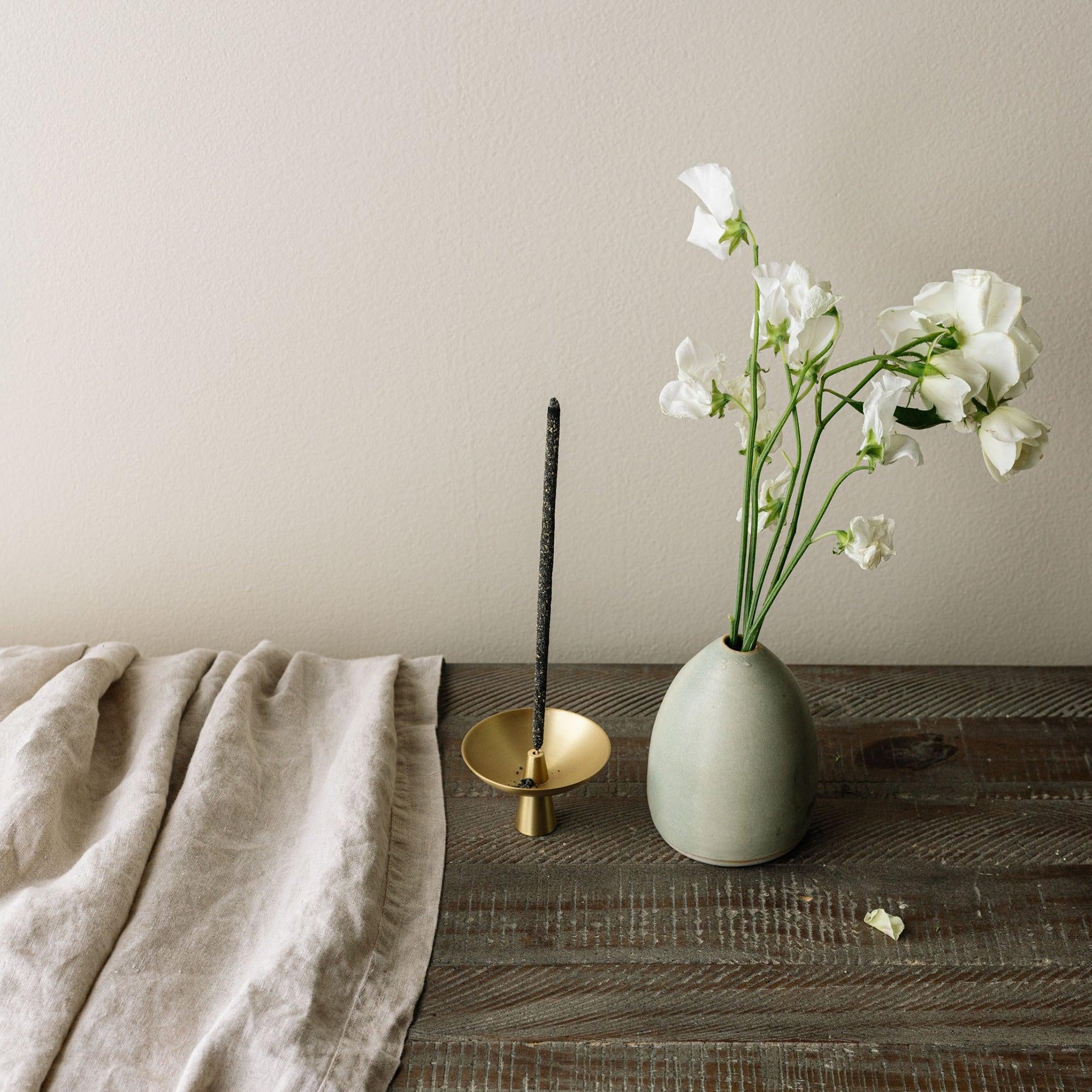 Vase with white flowers, candle holder, and beige towel on a wooden surface.