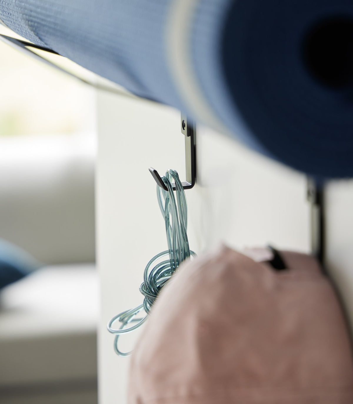 Close-up of the black Yamazaki Home Over-the-Door Fitness Equipment Hanger - Steel hooks beneath a blue mat, with a coiled turquoise jump rope and pink cap hanging from separate hooks.