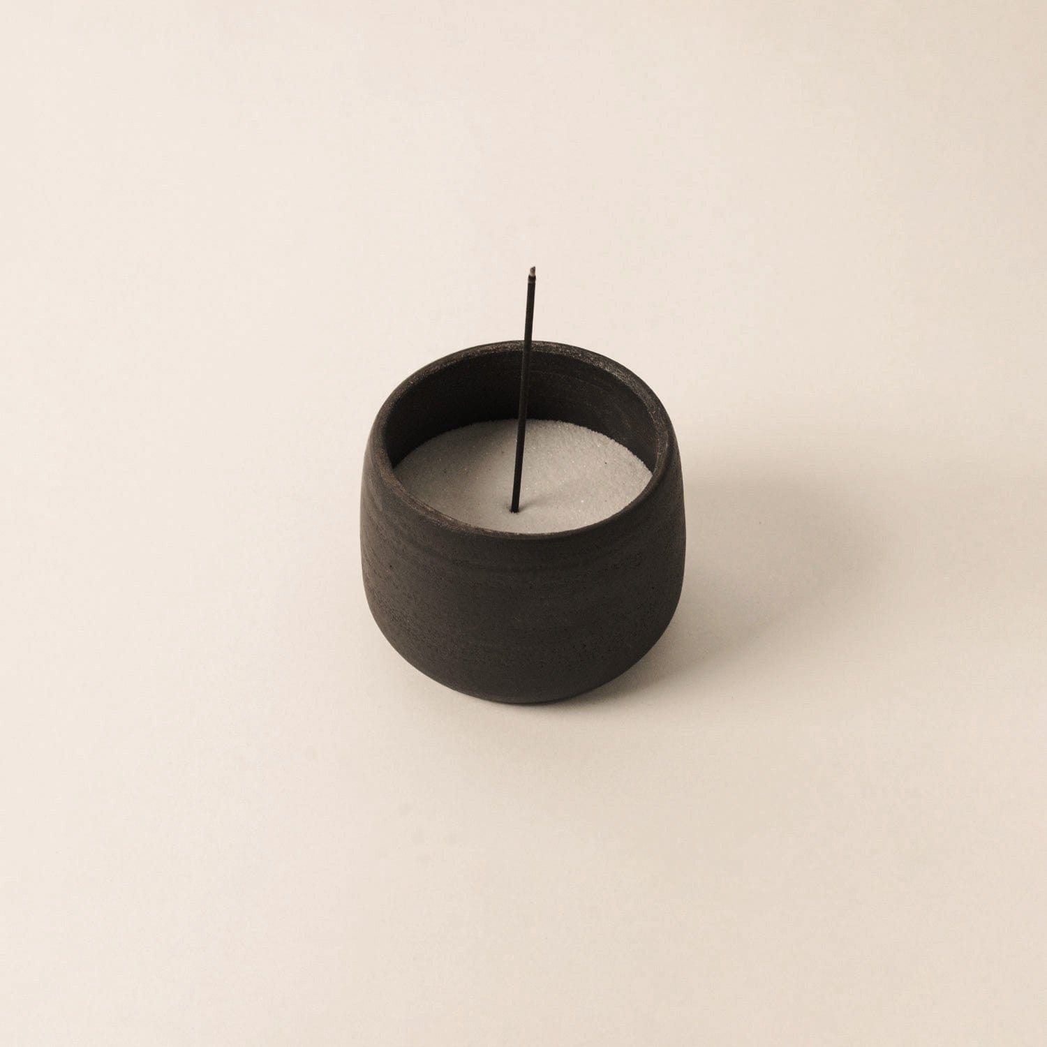 Black incense holder with a single incense stick on a beige background