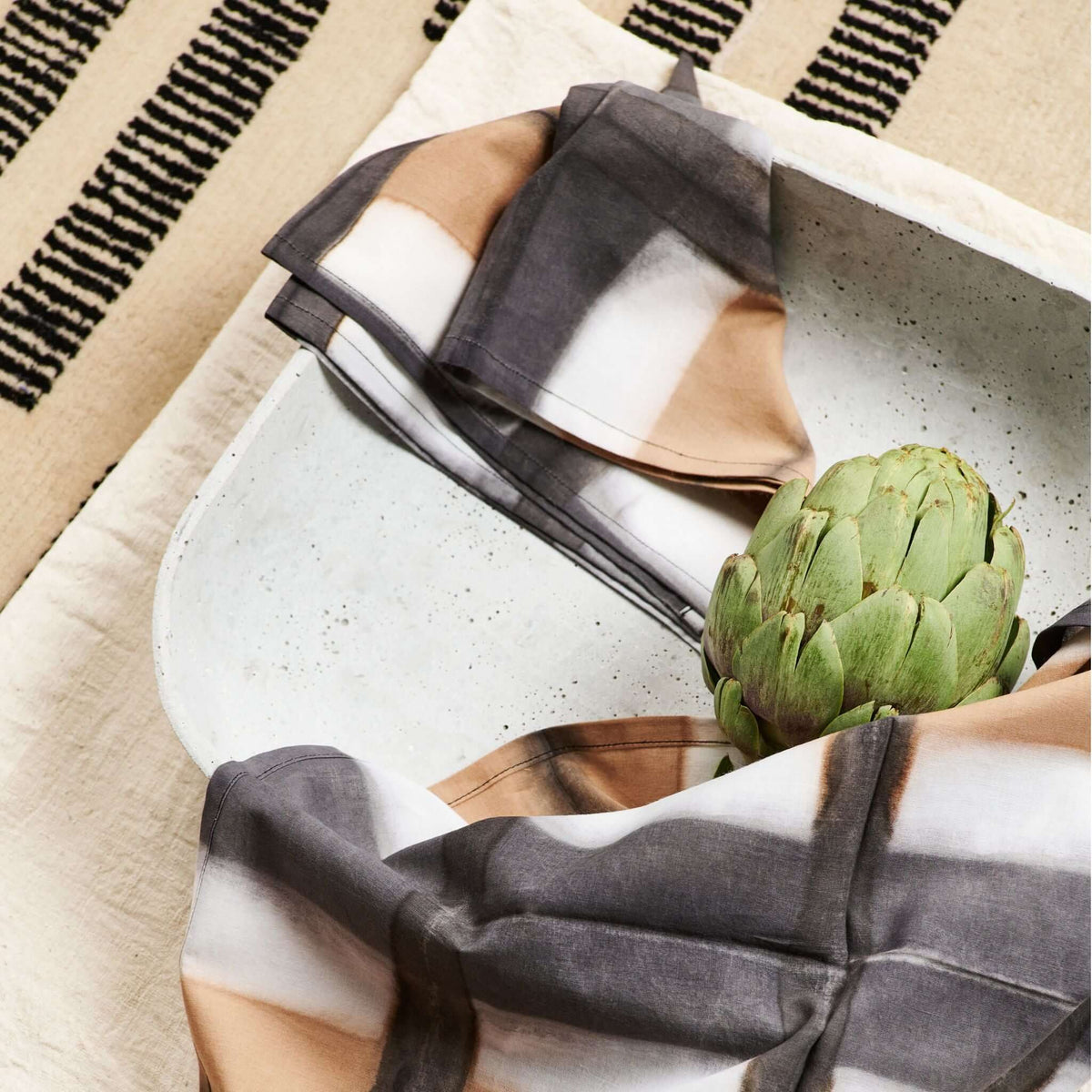 Close overhead view of Chowk Black napkins surrounding a ceramic plate and artichoke on a patterned table covering
