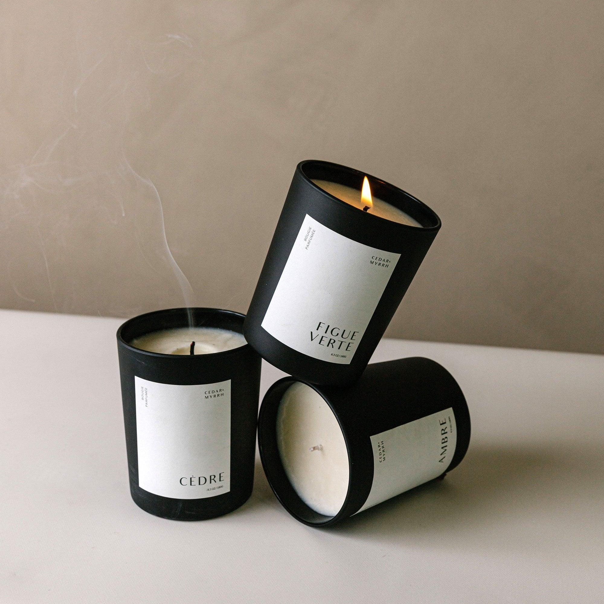 Three black candles with white labels on a neutral background