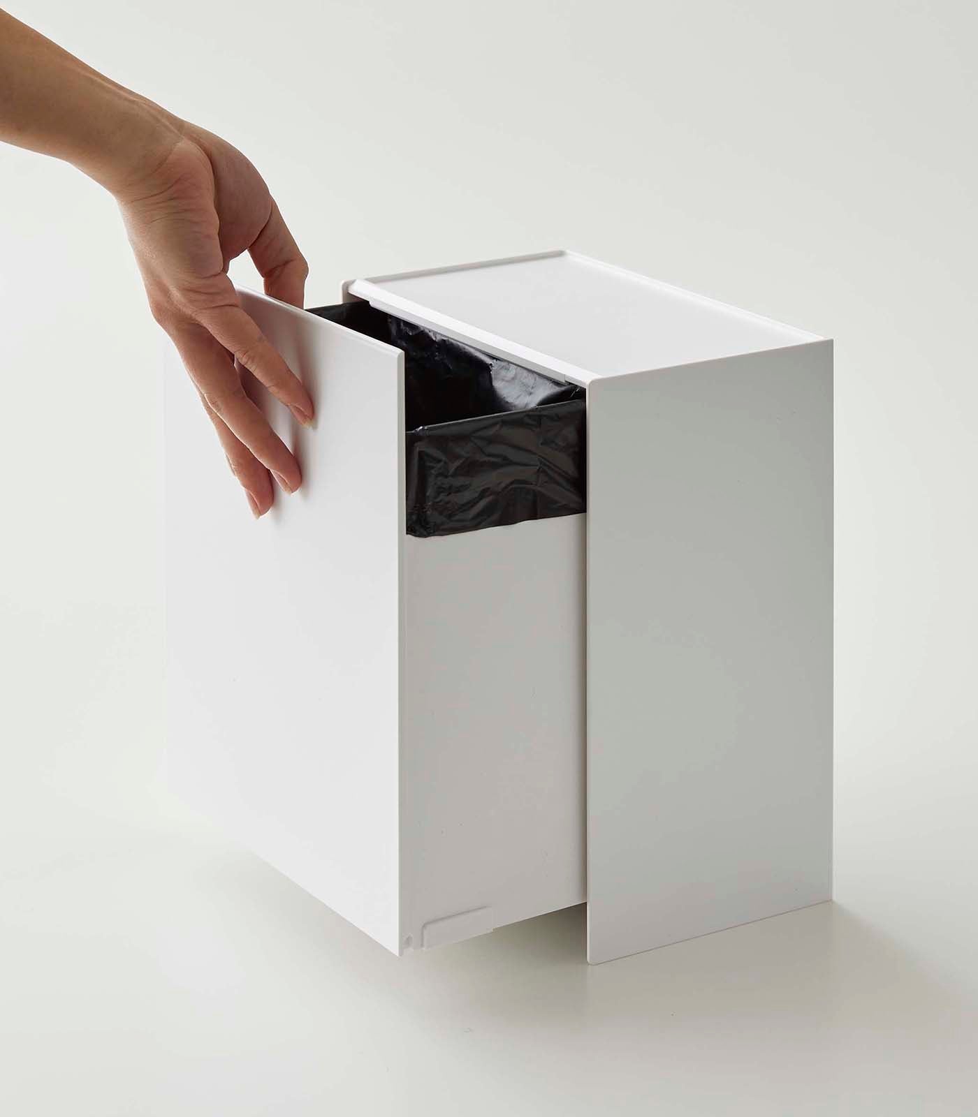 White trash bin with a hand opening the lid on a light gray background