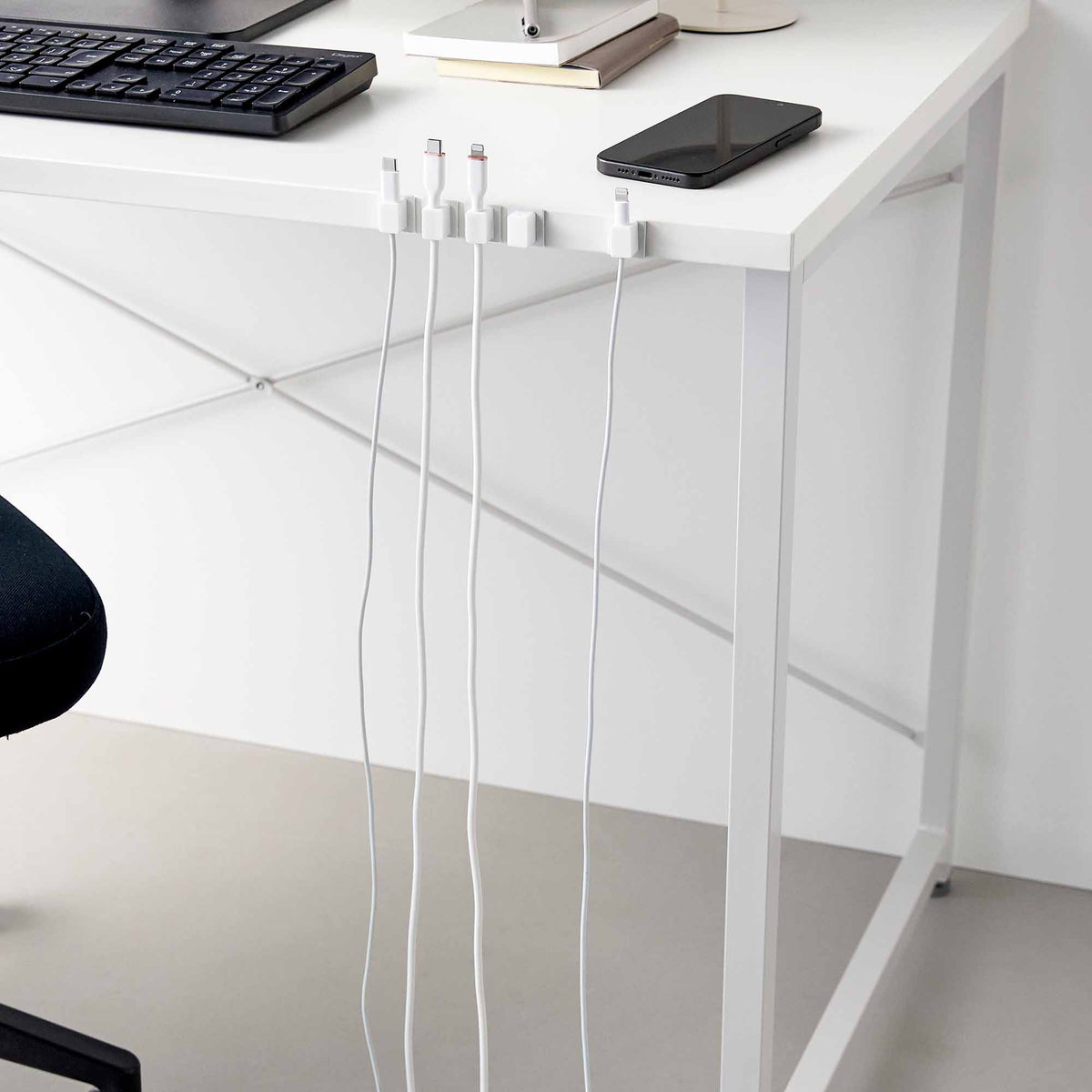 Wider view of white Yamazaki Home Magnetic Cable Holders With Adhesive Steel Bases (Set of 5) - Silicone along a desk edge, with charging connectors upright and cables hanging separately toward the floor.
