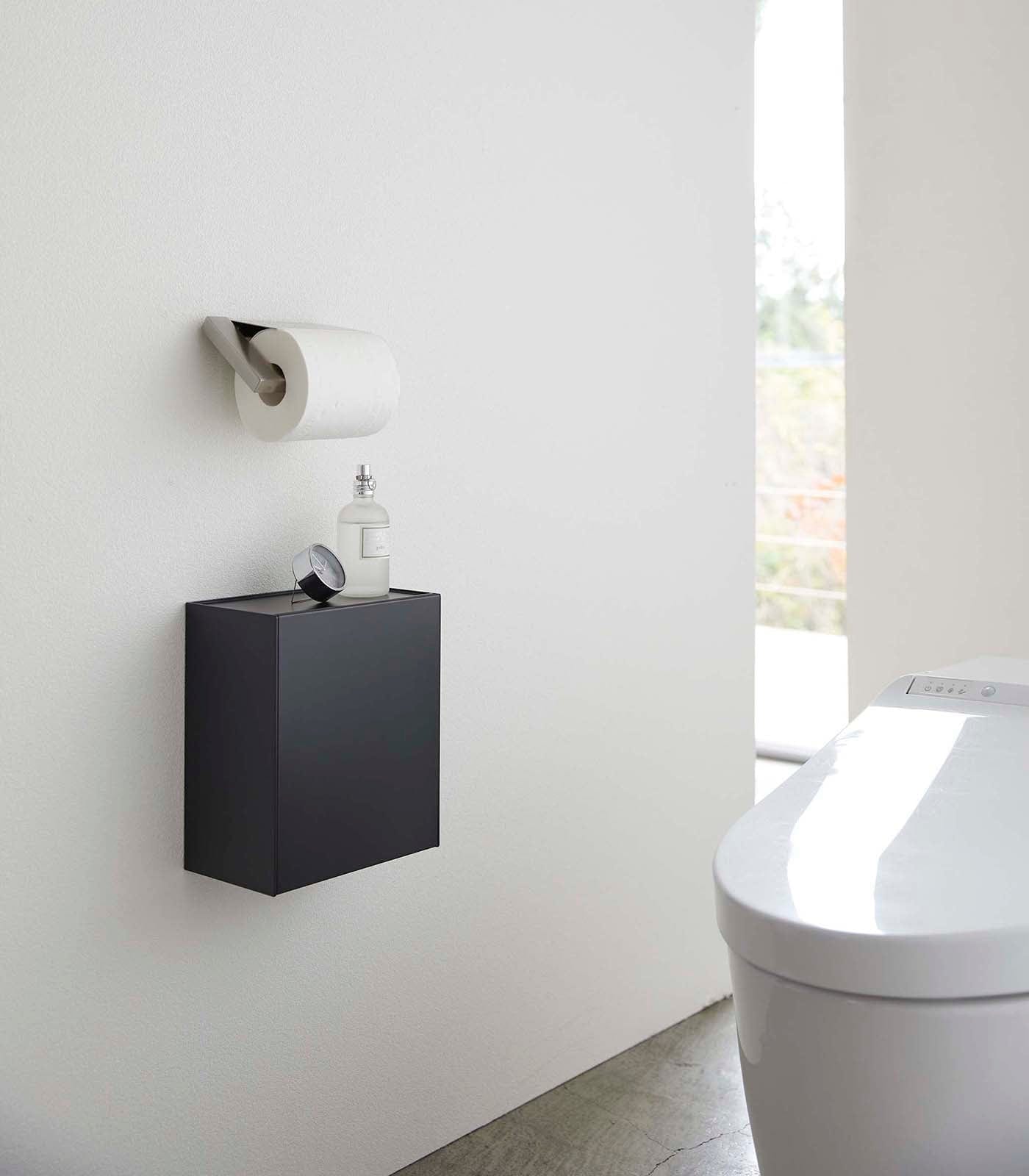 Modern bathroom with a black wall-mounted cabinet, toilet paper holder, and toilet.