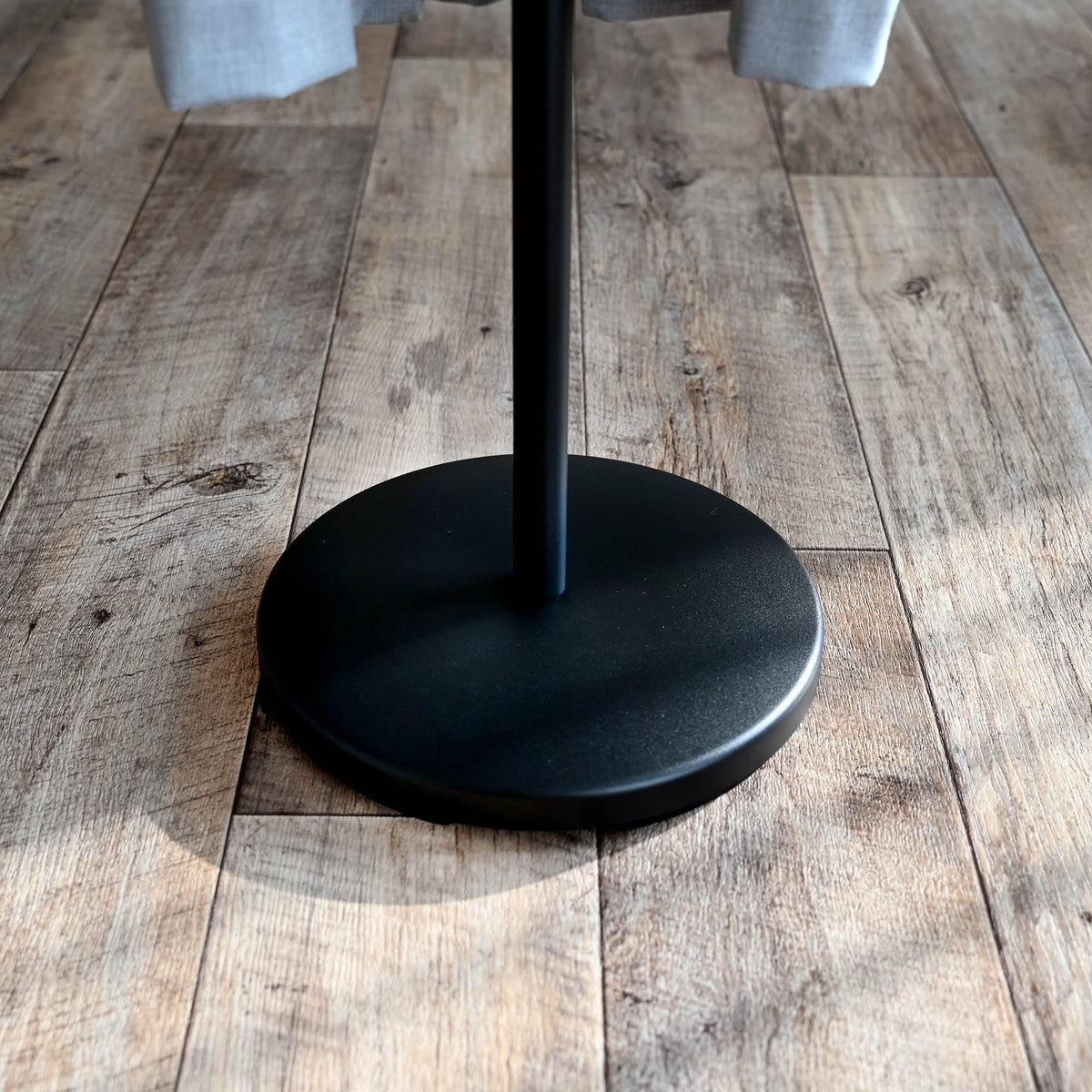 Black Yamazaki Home Coat Rack (70" H) - Steel base shown close up on wood flooring, with a broad circular foot supporting the narrow central pole.