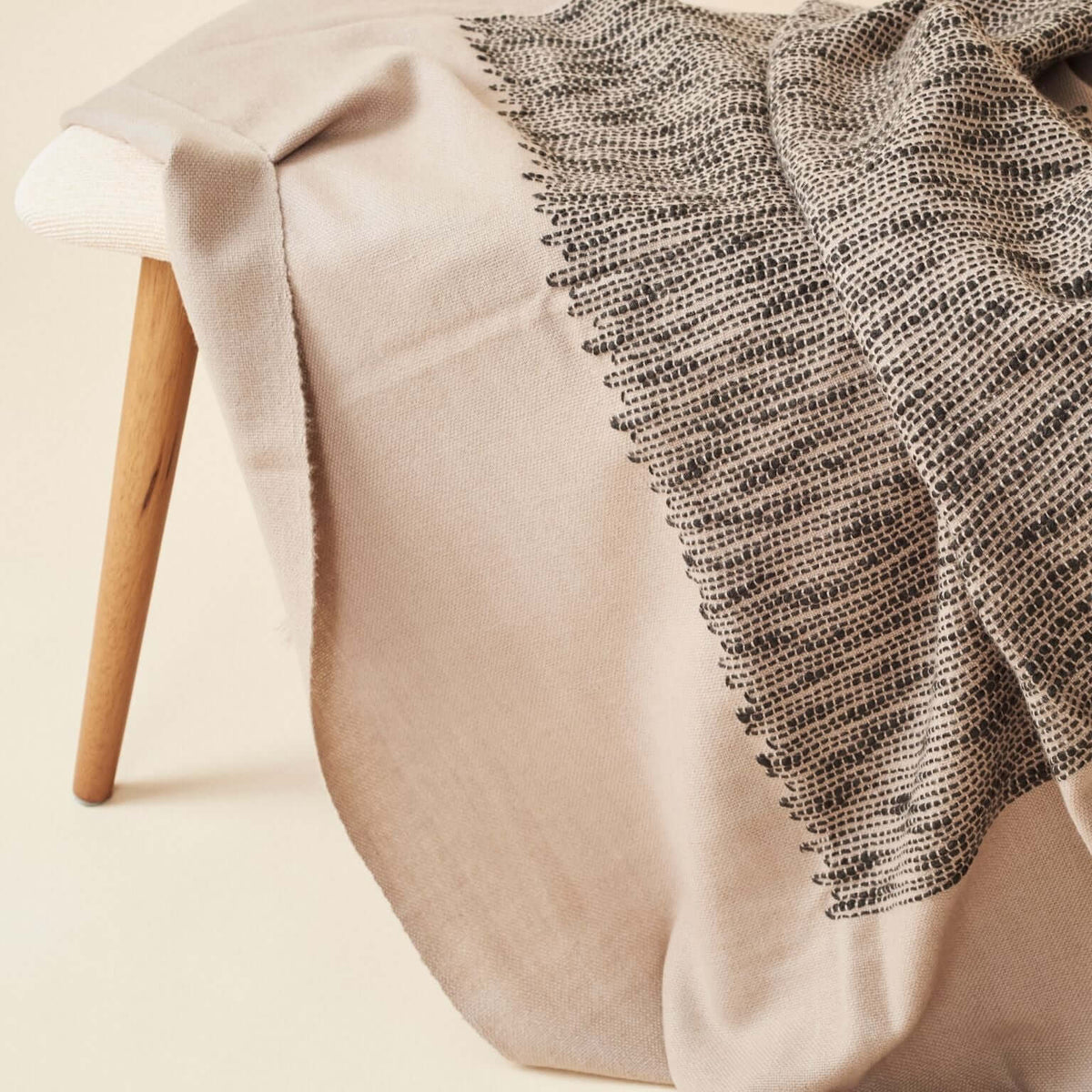 Close lifestyle view of the Flo Brown throw cascading over a pale wood bench with its dark woven pattern visible