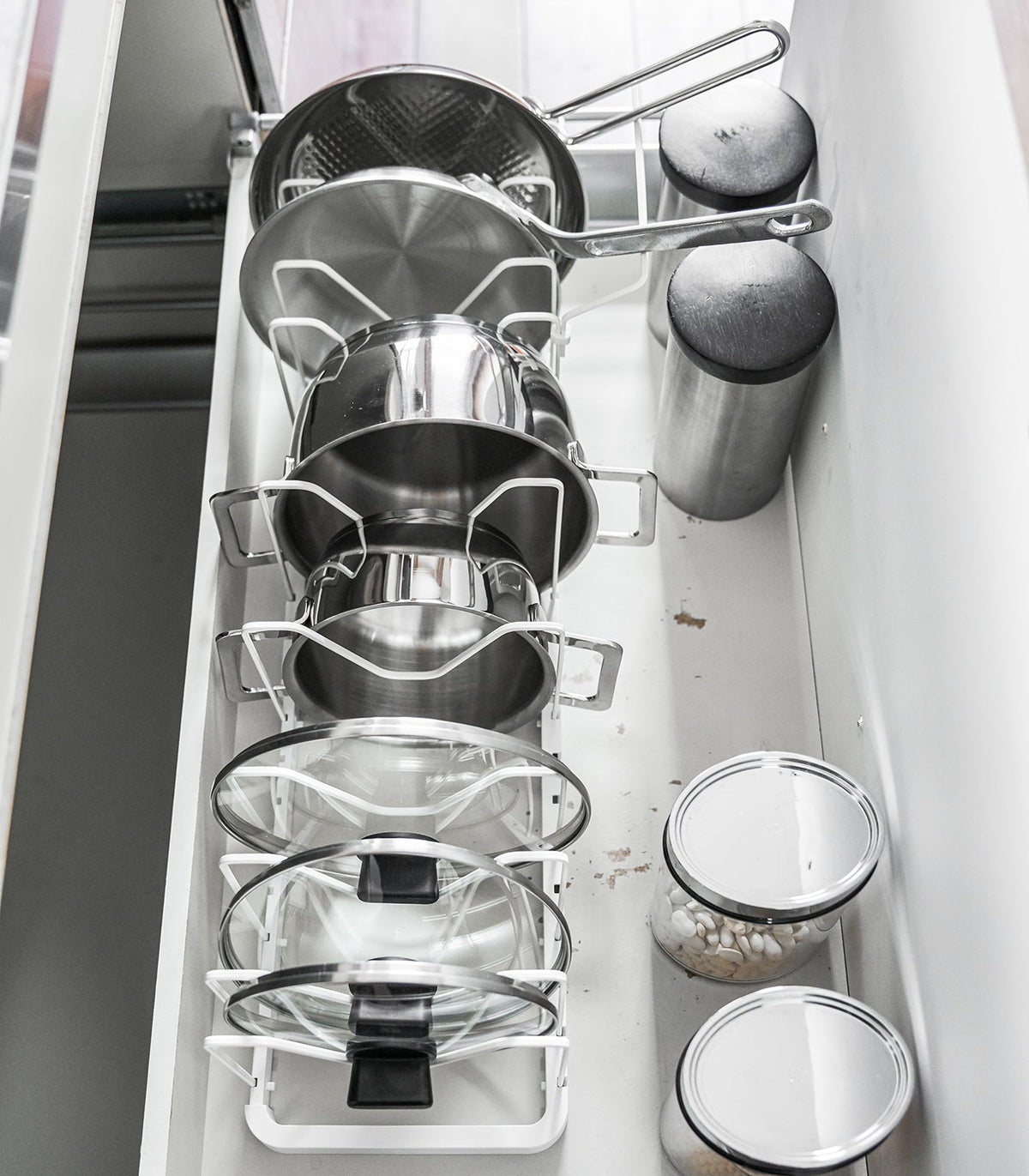 Overhead view of the white Yamazaki Home Adjustable Pot Lid Organizer - Steel in a drawer, showing cookware stored upright in individual slots with handles extending toward the back.