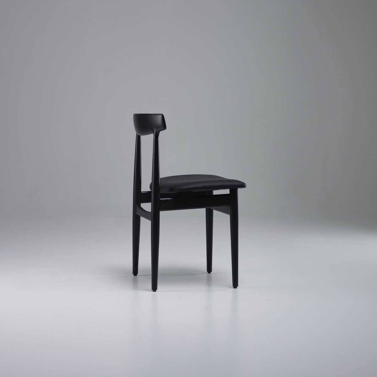 Side view of the black Eikund Hertug Dining Chair in a gray studio, showing its slightly reclined backrest, thin seat, and open frame.