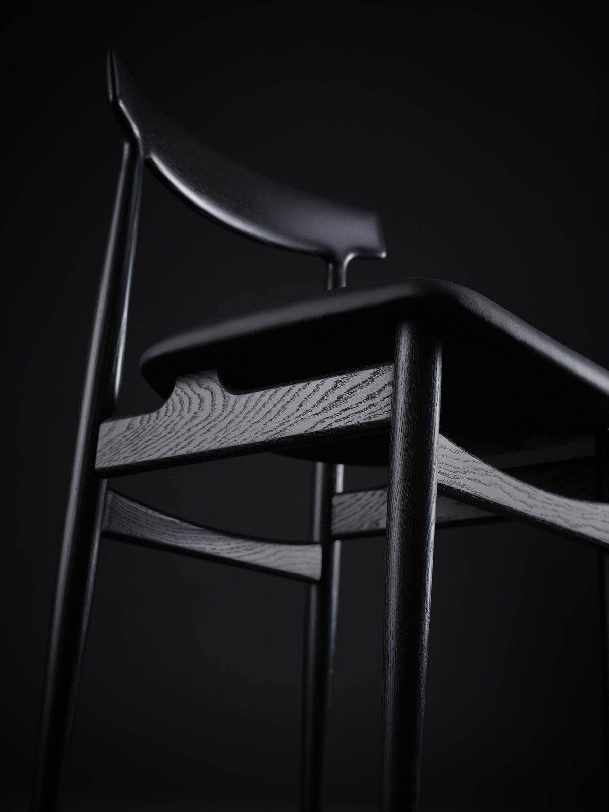 Low-angle detail of the black Eikund Hertug Dining Chair, showing the curved backrest, rounded seat edge, and grain-patterned side rail joining the legs.