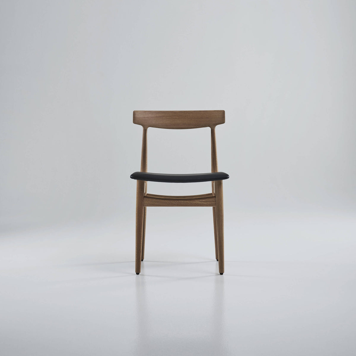 Front view of the Eikund Hertug Dining Chair with a light brown wood frame and black seat in a gray studio, showing its curved wood backrest and slim legs.