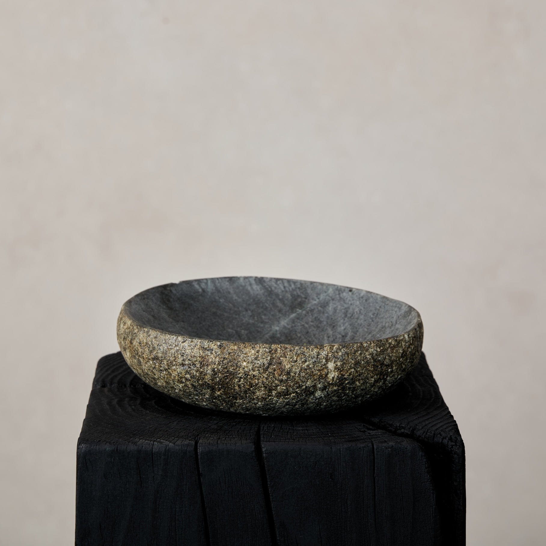 Natural stone bowl on a black stand against a beige background