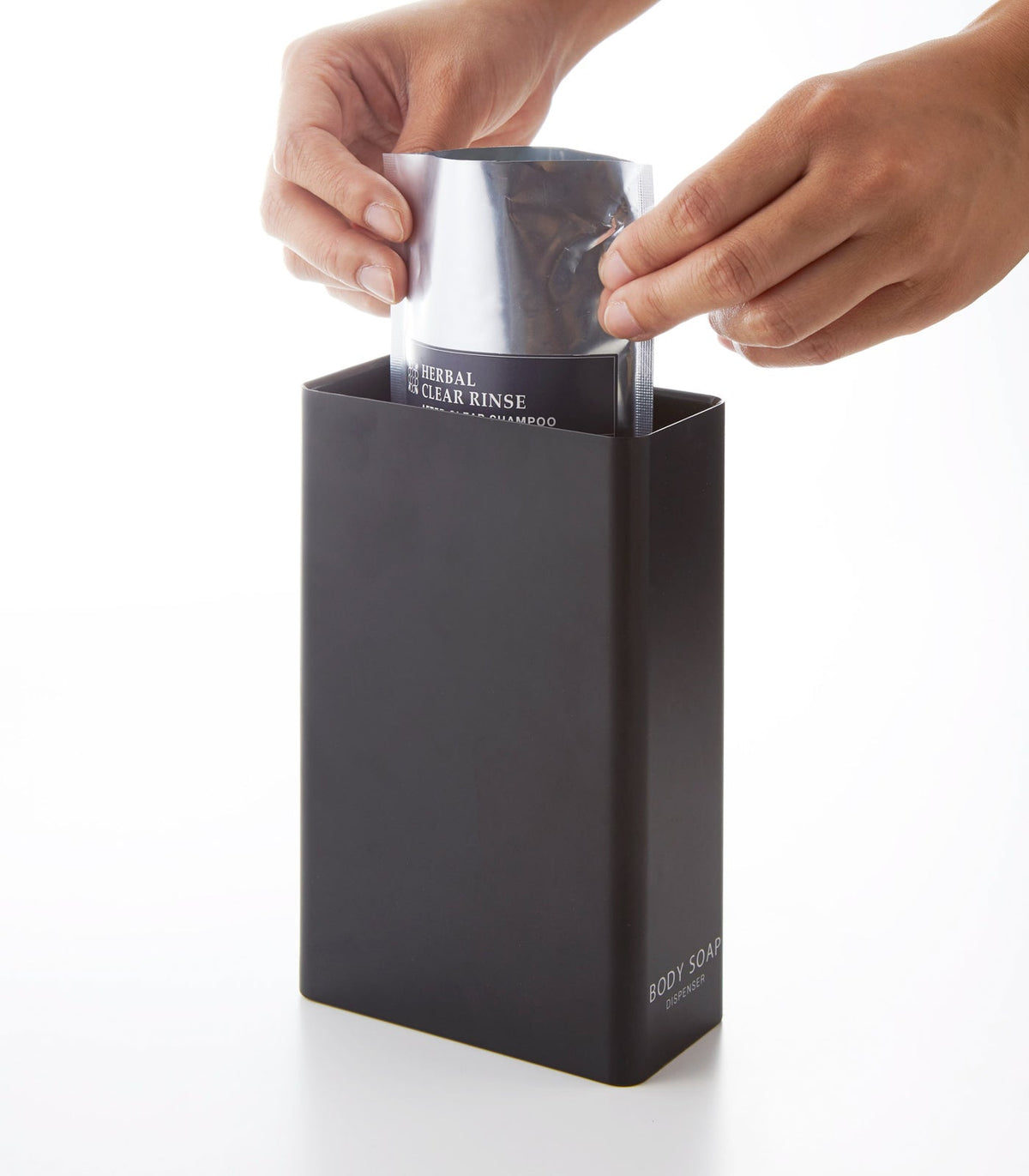 A person inserts a refill pouch through the wide open top of the black Yamazaki Home Rectangle Shower Dispenser - Three Styles.
