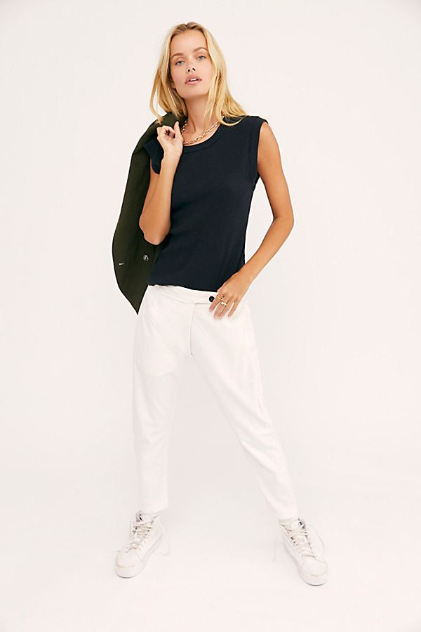 Model wearing white Canvas Souk pants with a black sleeveless top and white sneakers.