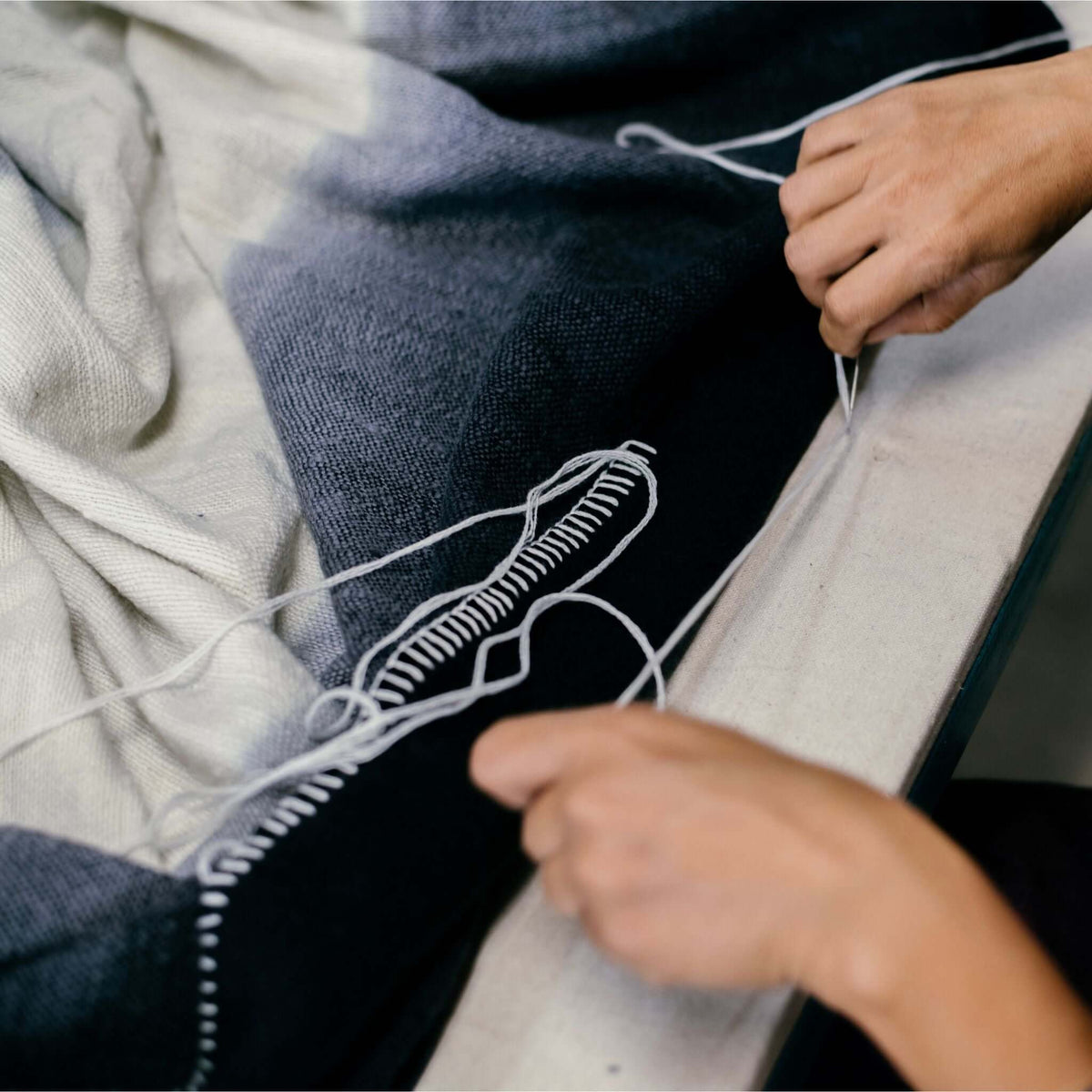 Detailed overhead view of hands forming the decorative white looped stitching along the throw’s dark border