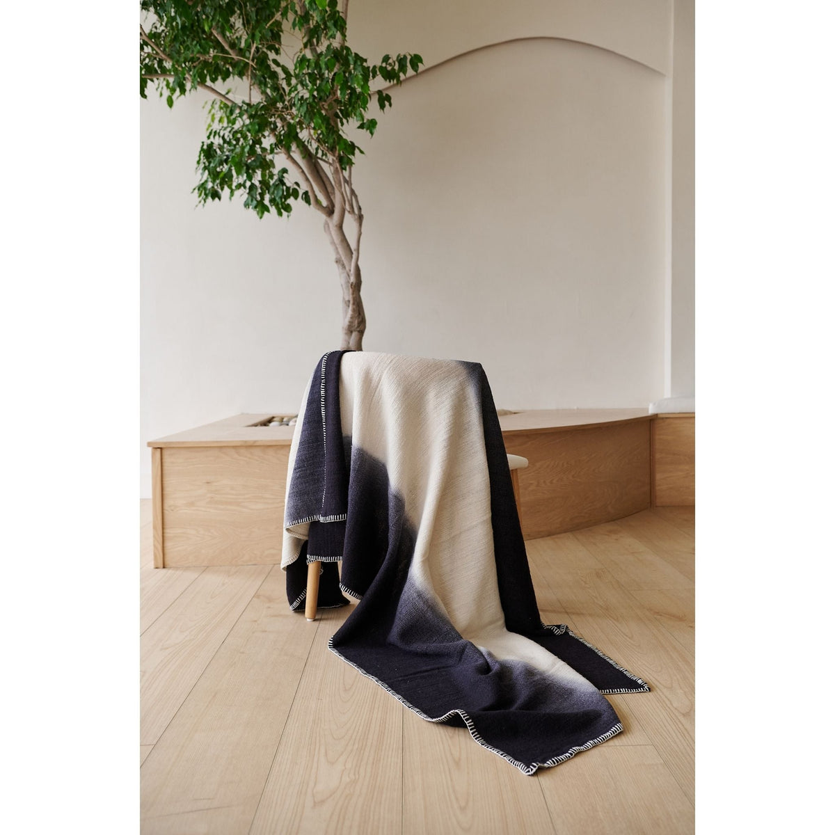 Ink Black and White handwoven throw cascading from a chair onto a pale wood floor beneath an indoor tree