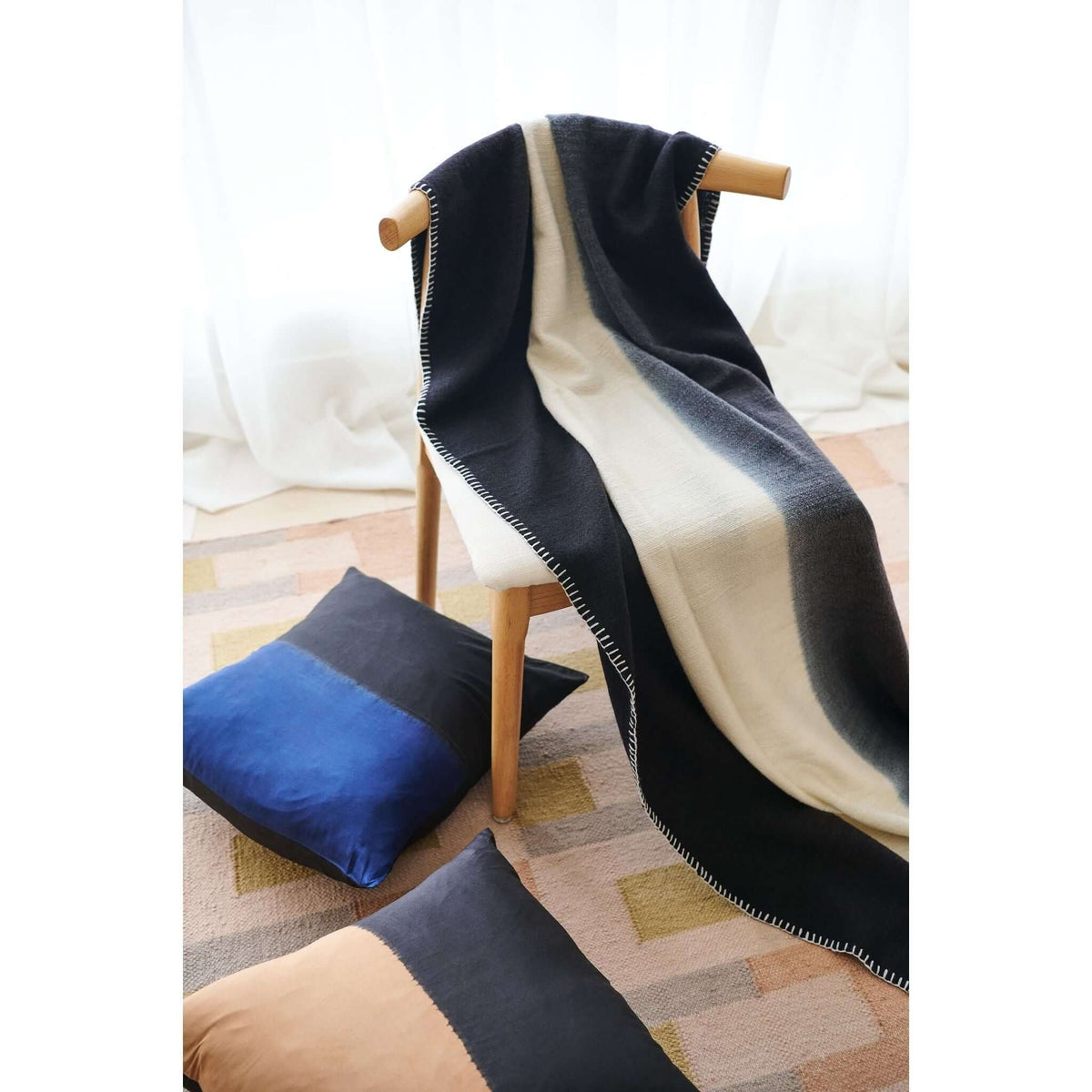Ink Black and White throw flowing over a wood chair beside blue and charcoal floor cushions
