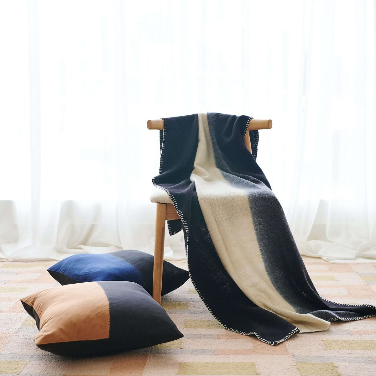 Full lifestyle view of the Ink Black and White merino blanket draped from a chair onto a patterned rug