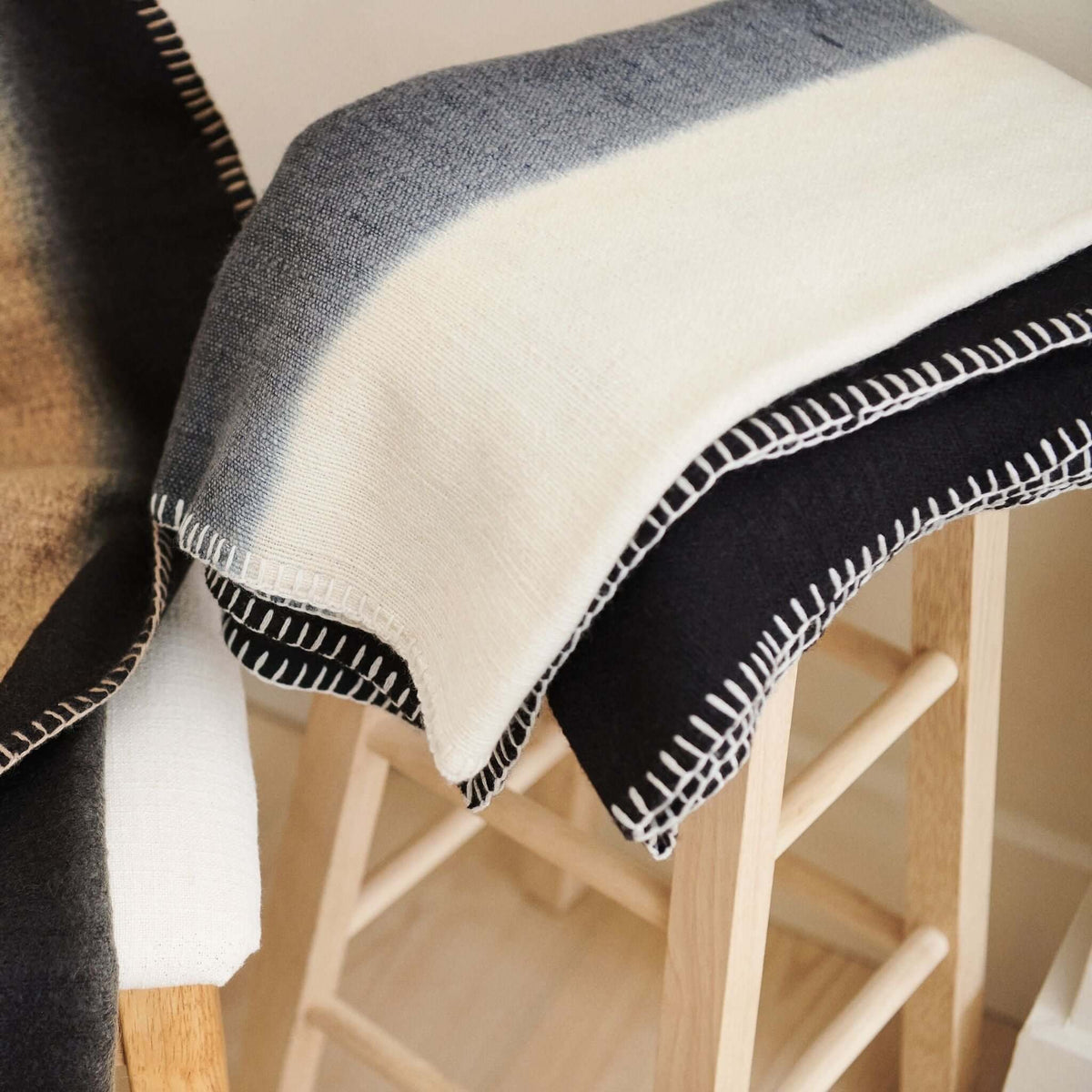 Close-up of the merino throw folded over a chair arm, showing the soft weave, wide cream stripe and white edge stitching