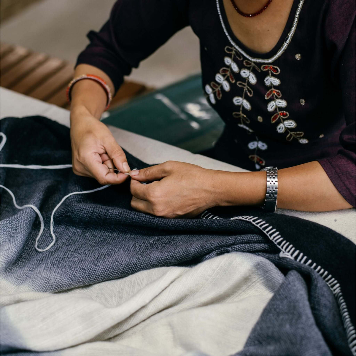 Close view of an artisan sewing the white blanket-stitch border onto the black merino wool edge