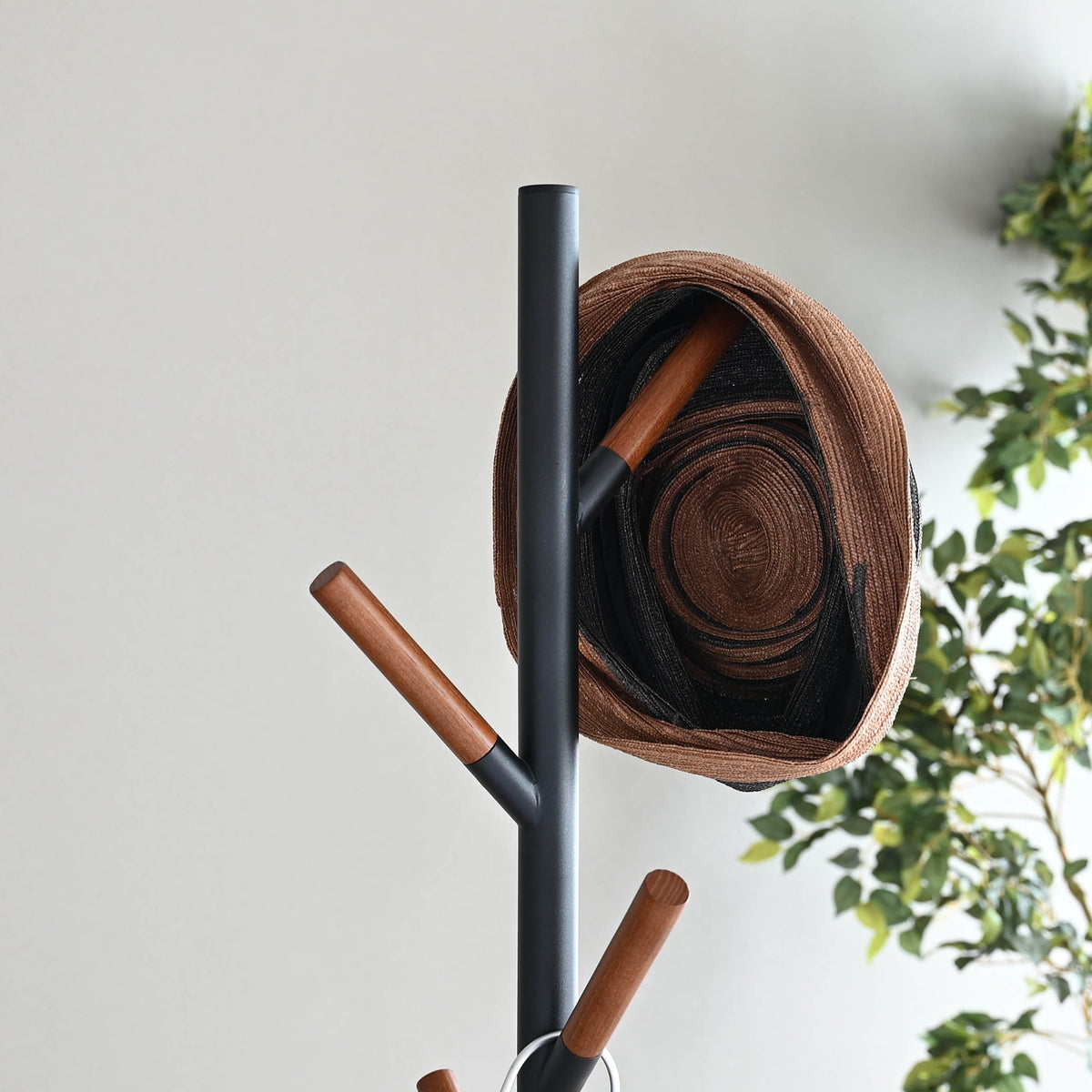 Close-up of the black Yamazaki Home Coat Rack (70" H) - Steel upper branches, with brown wooden tips and layered brown and dark hats.