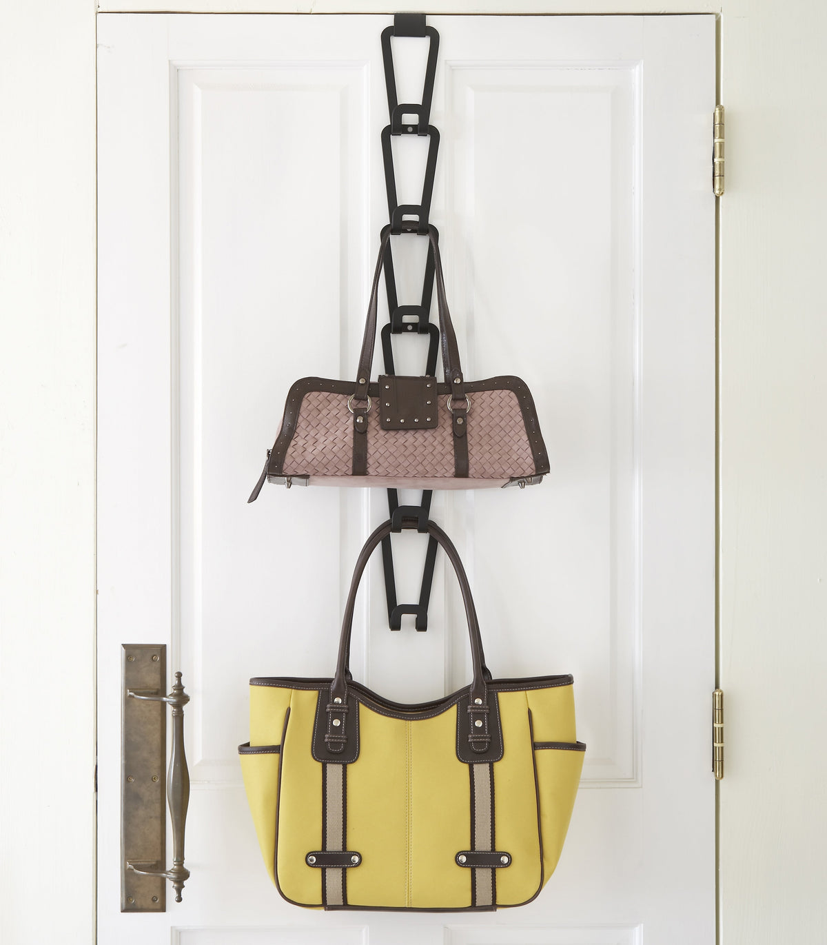Black Yamazaki Home Cascading Storage Hooks - Steel on a white door, with several empty links above a patterned handbag and a large yellow tote hanging below.