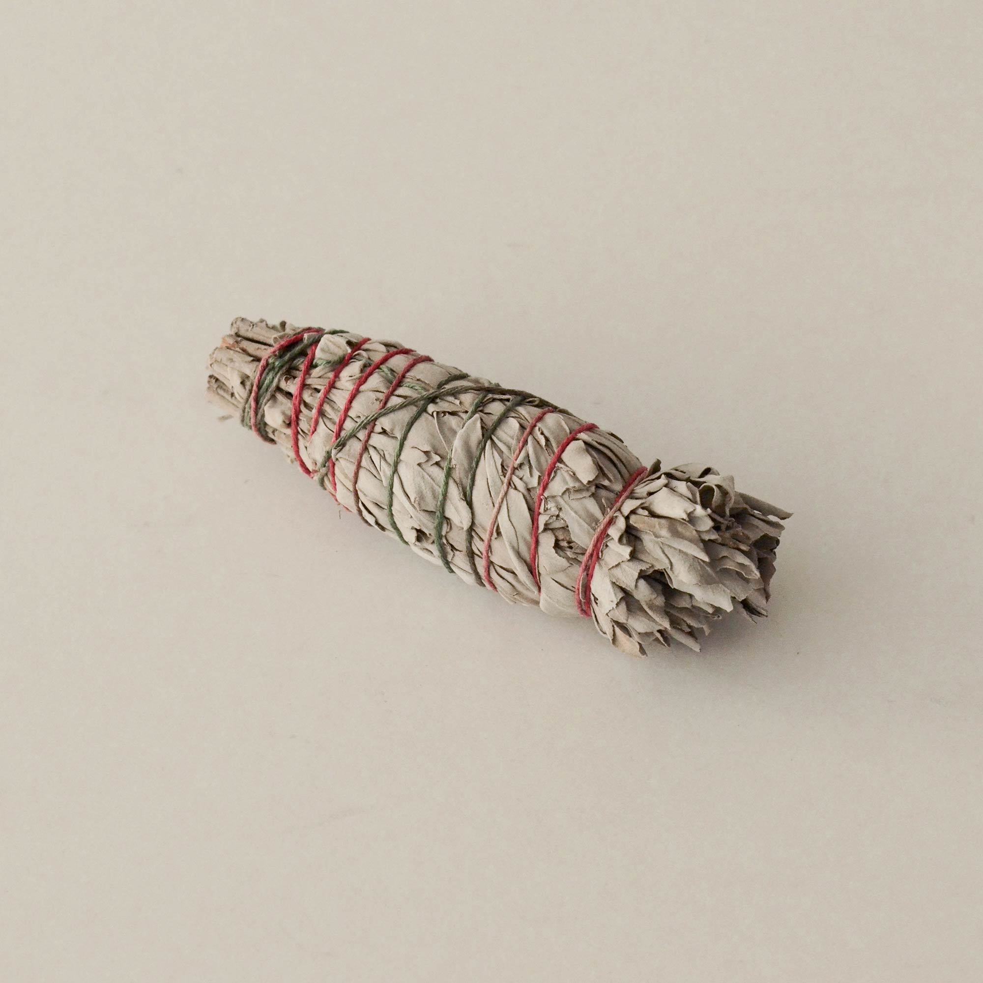 Bundled sage stick with red string on a beige background