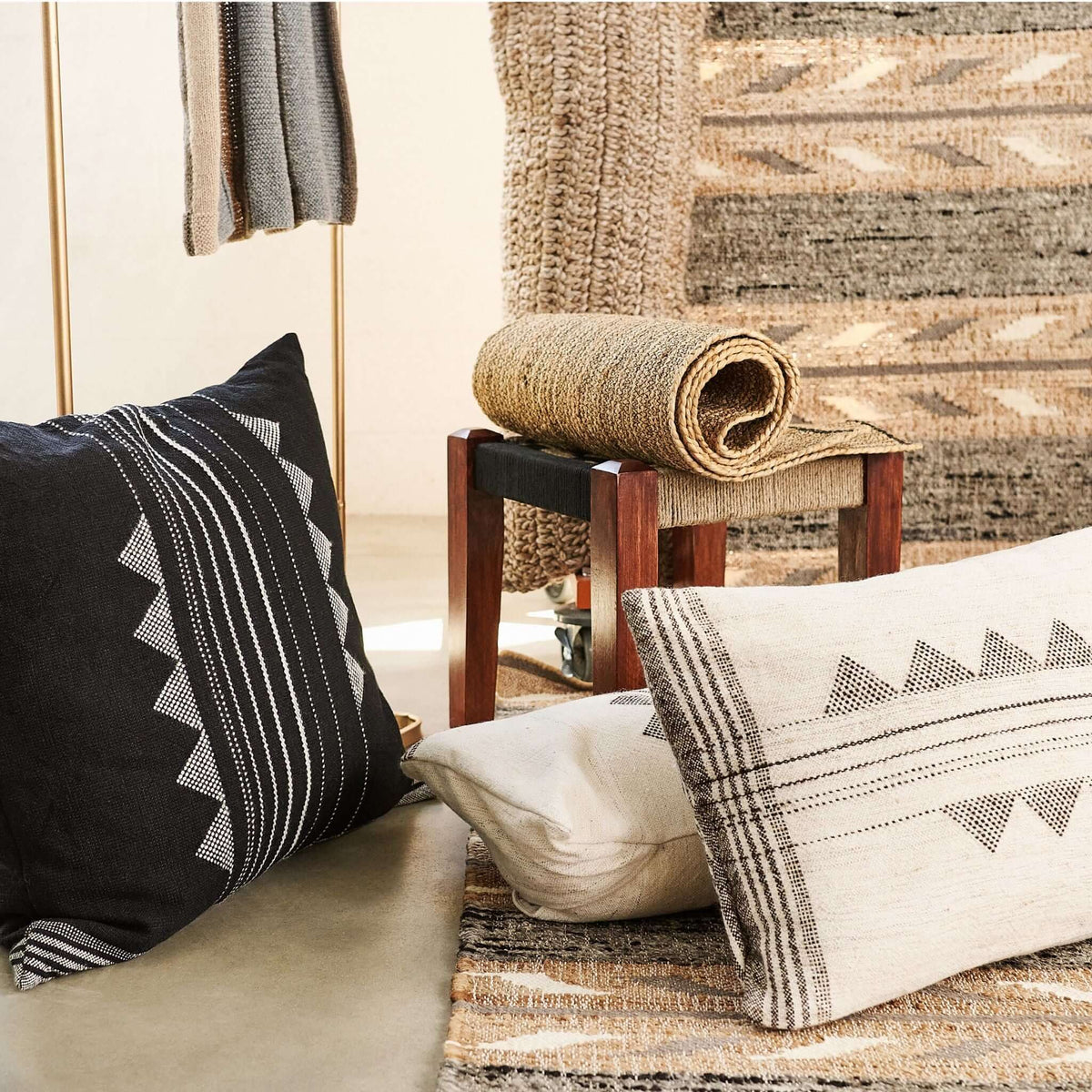 Kora Black and ivory handloom pillows displayed with rolled rugs and woven textiles in an artisan shop