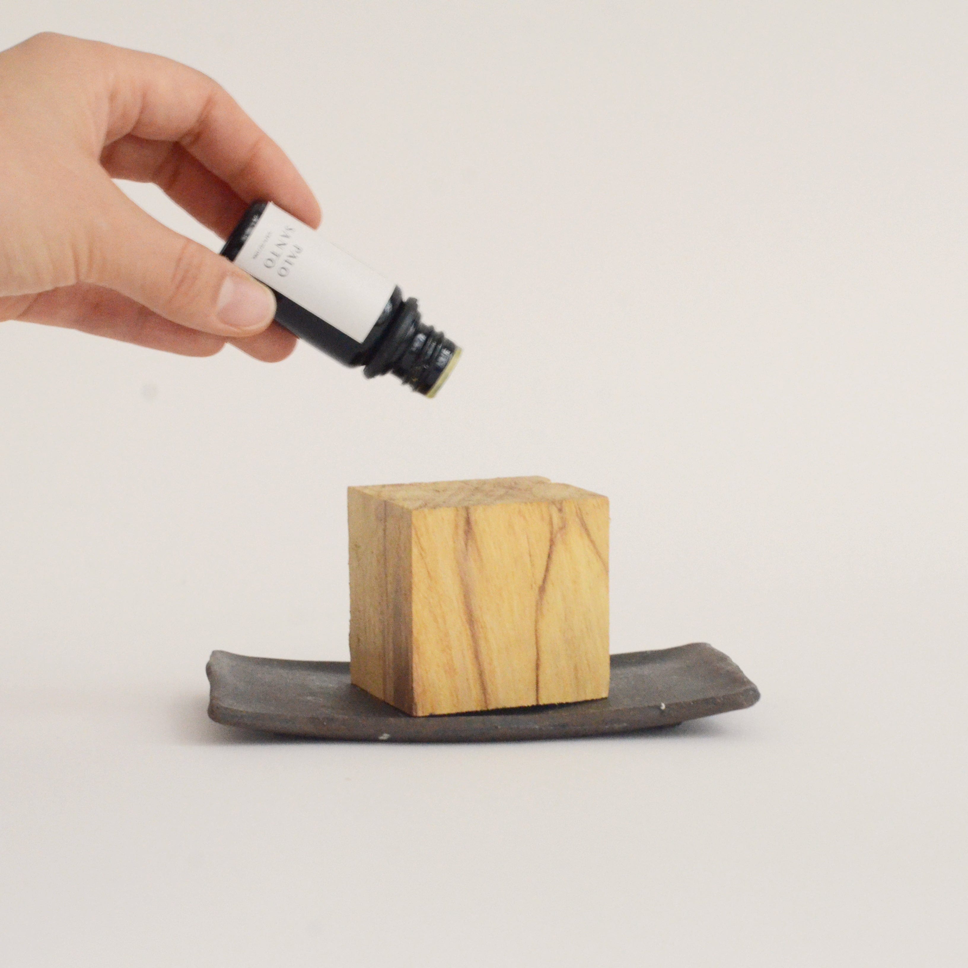 Hand holding a small bottle over a wooden block on a stone surface with a plain background
