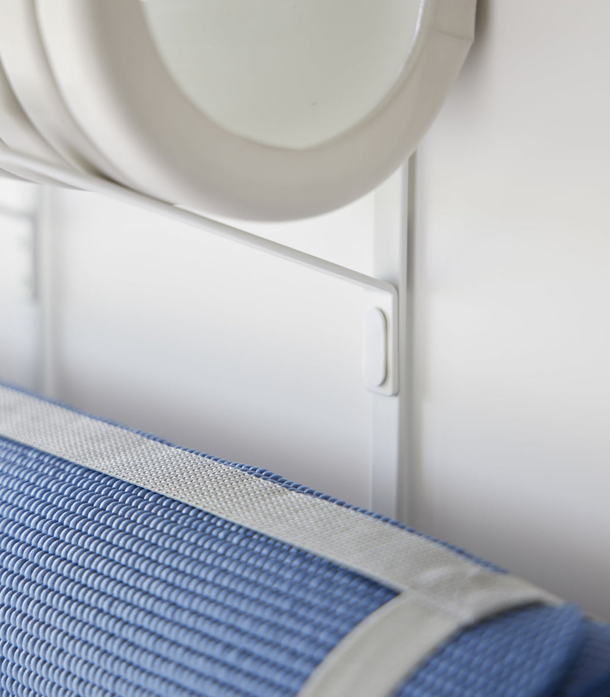 Close-up of the white Yamazaki Home Over-the-Door Fitness Equipment Hanger - Steel upright and support connection, framed by the grey foam roller above and blue mat below.