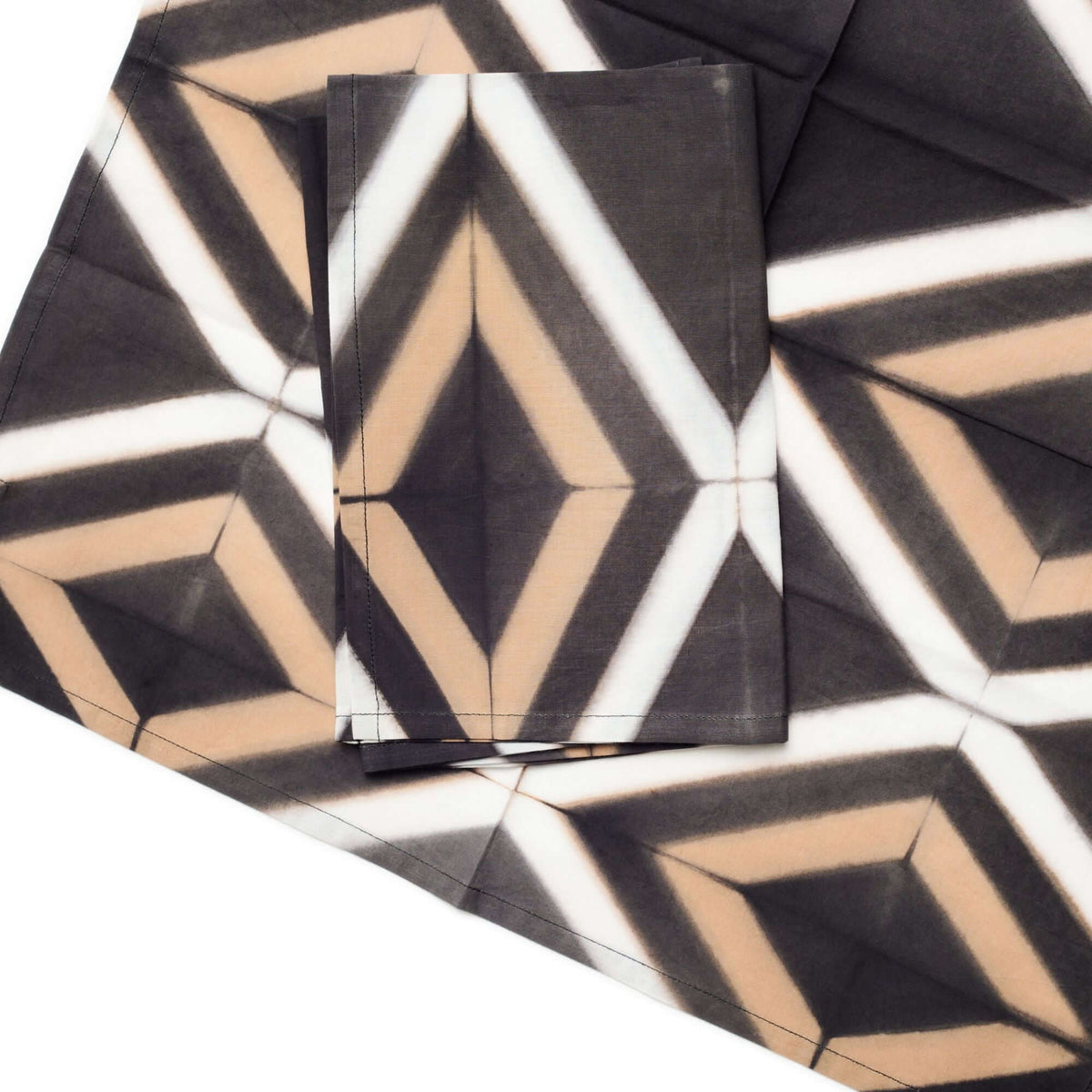 Close-up of folded Tisa napkins showing the sharp diamond shapes and hand-dyed color variations.