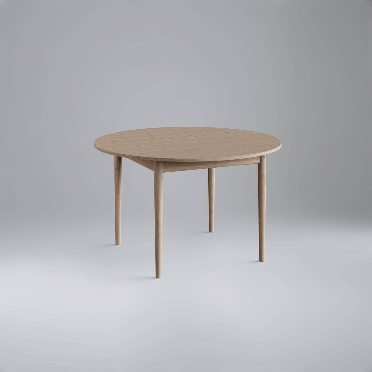 Three-quarter view of the light wood Eikund Oma Static Dining Table in a gray studio, showing the circular top, recessed apron, and four tapered legs.