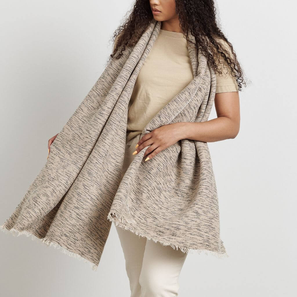 Woman wearing the oversized neutral scarf open over a cream outfit.