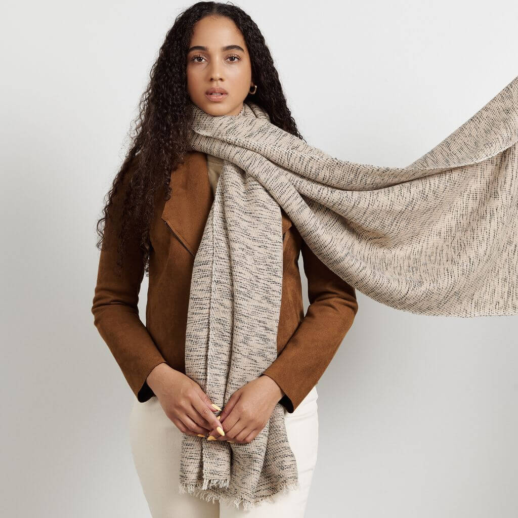 Woman in a brown jacket styling the long fringed scarf around her neck and shoulders.