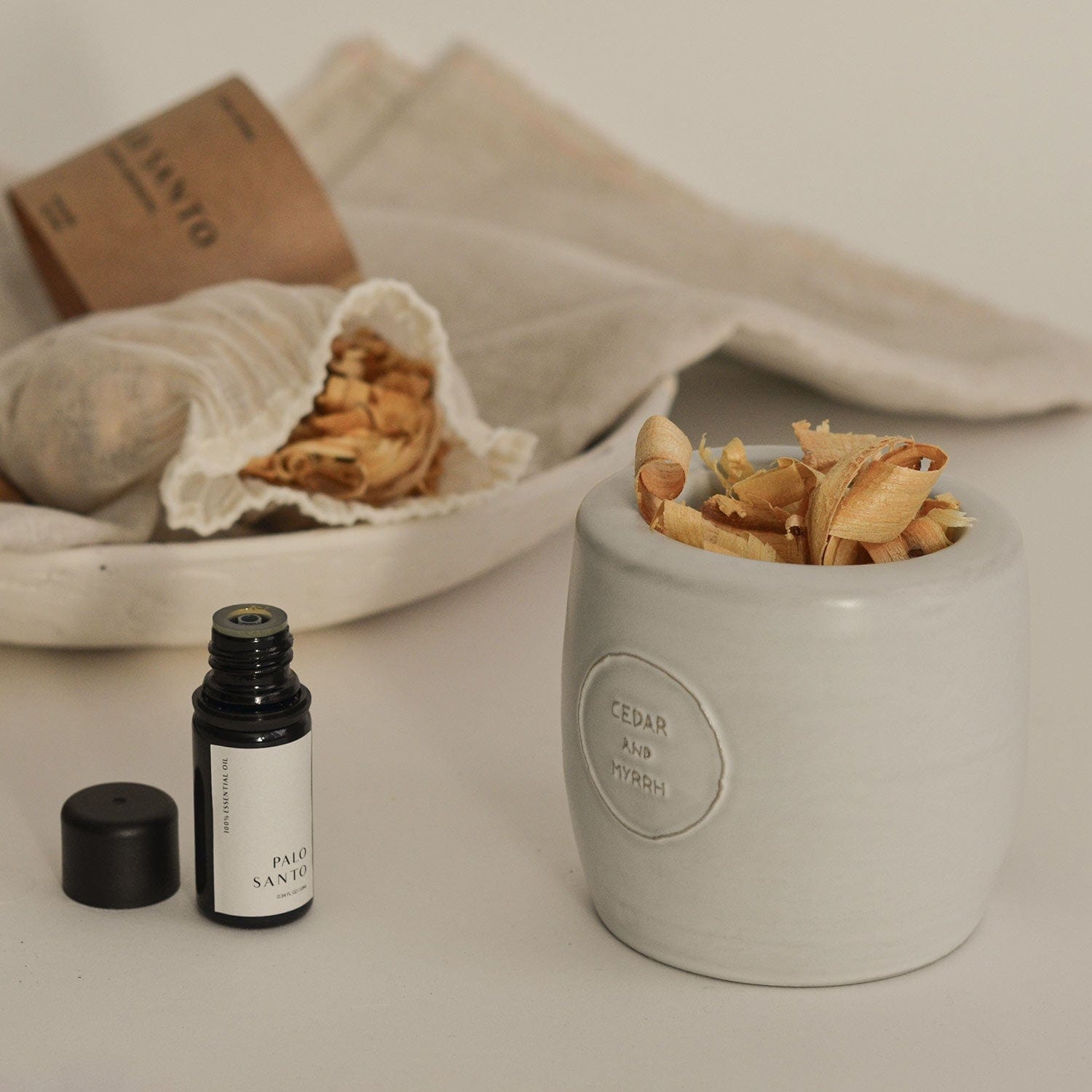 Small bottle of Palo Santo with a ceramic container holding dried Palo Santo wood on a neutral background.