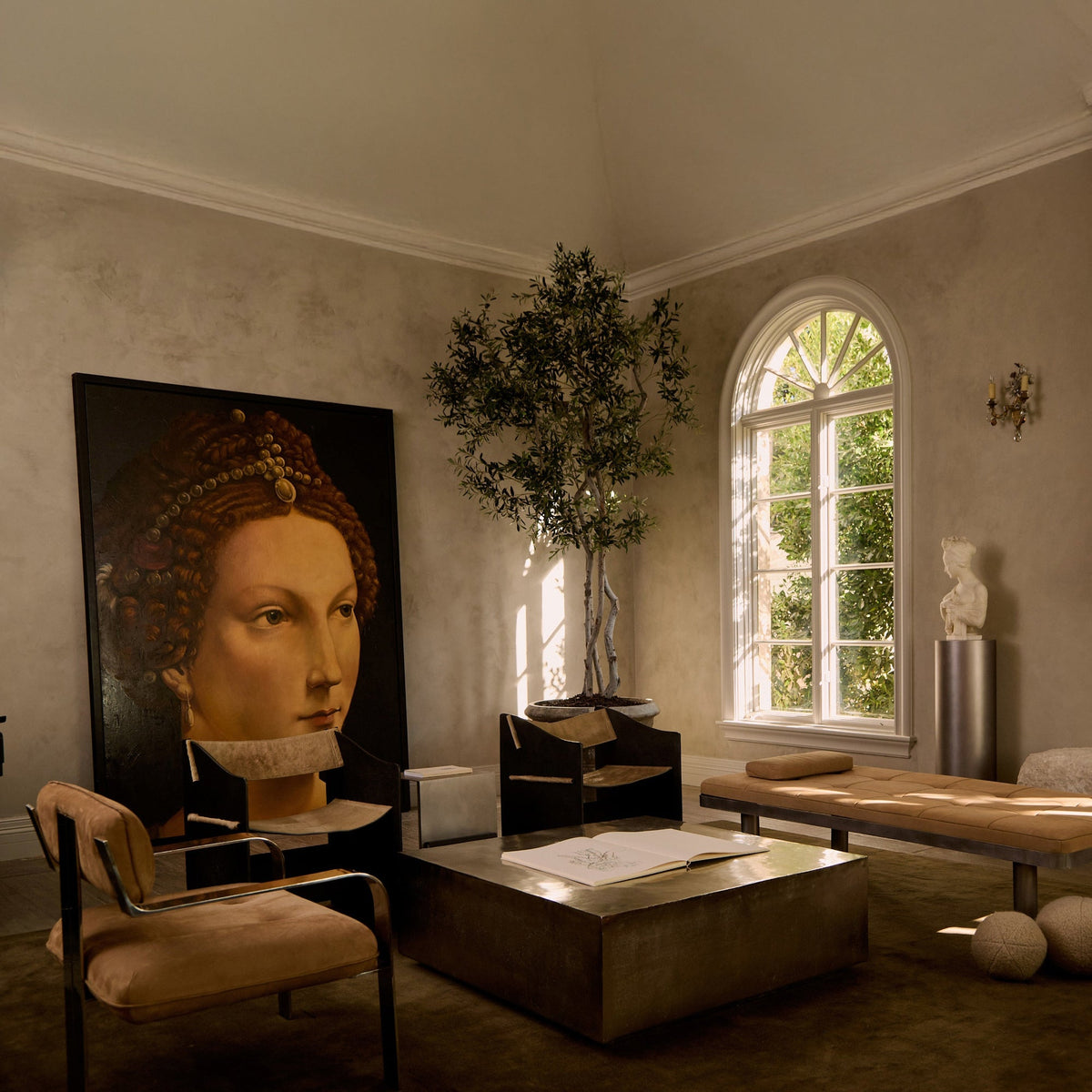 Living room with a large portrait of a woman on the wall, a coffee table, and a window with plants.