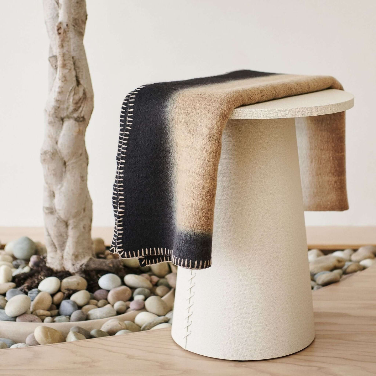 Close-up of the Siro Brown throw’s black border, tan center and contrasting looped stitching over a white stool