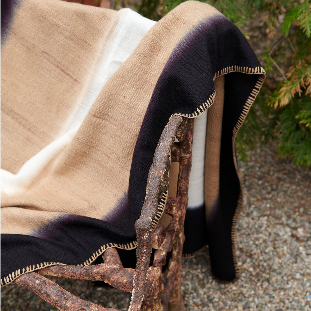 Siro Brown throw draped over an outdoor wood chair, highlighting its soft tan weave, black border and hand stitching