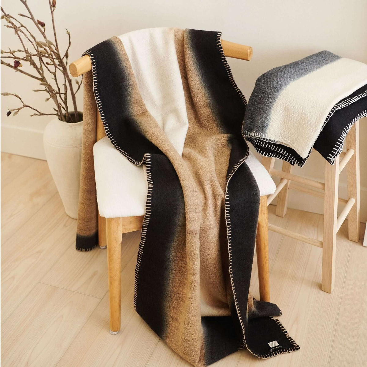 Wider room view of the Siro Brown throw draped over a chair with a second neutral blanket displayed nearby