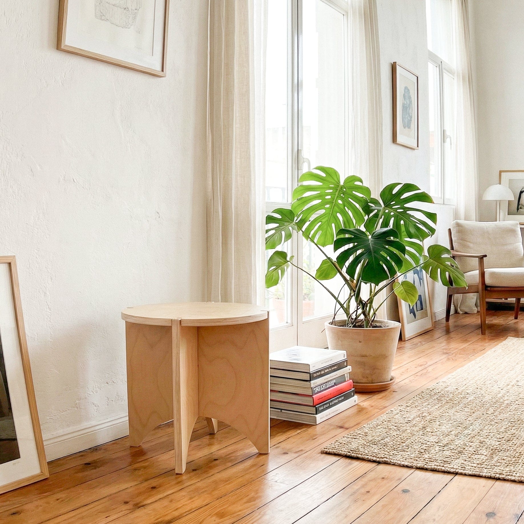 YOYO wood end table against a sunlit wall beside stacked books, a large leafy plant and a woven rug