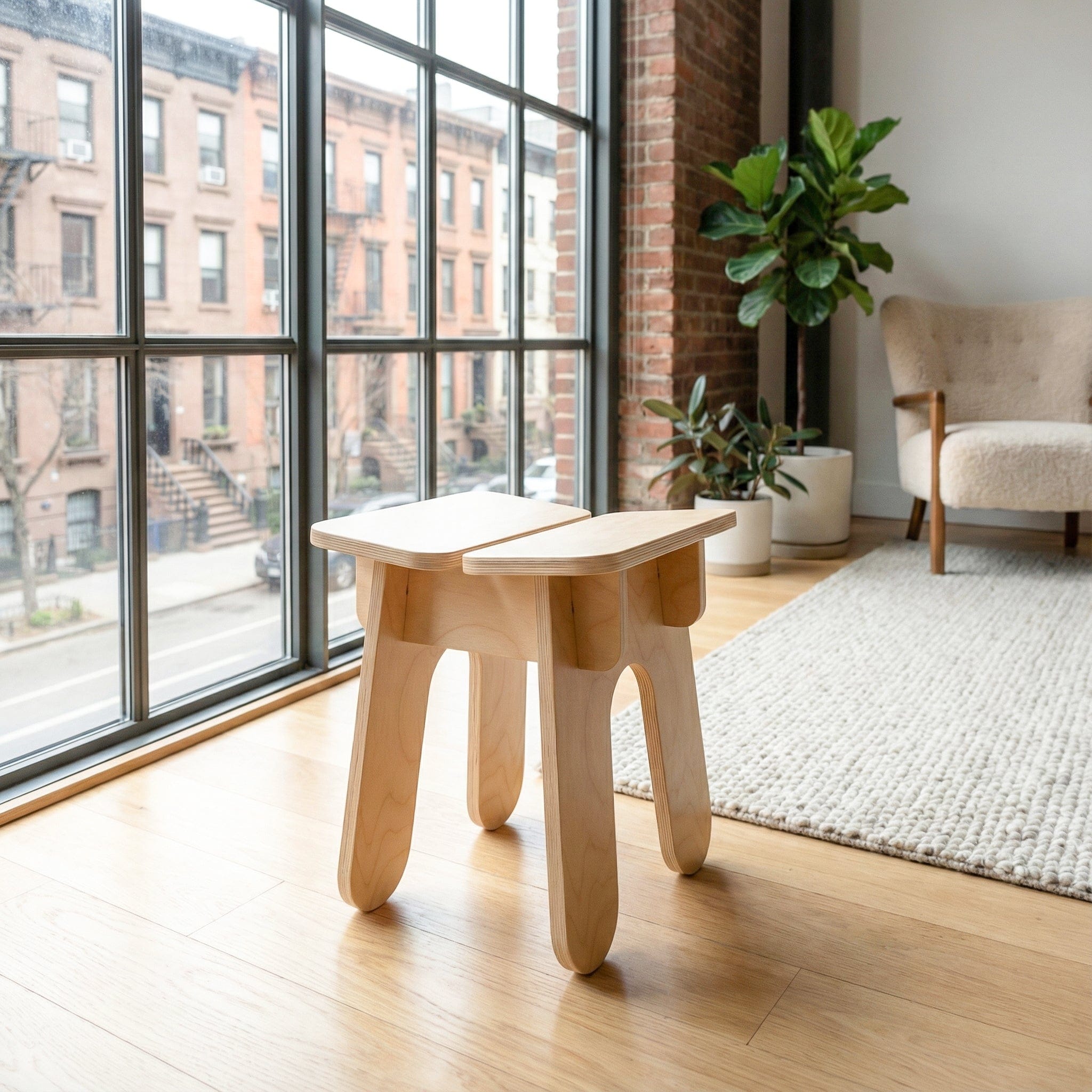 BURIJ natural wood stool in a bright loft beside floor-to-ceiling windows, a leafy plant and a woven rug