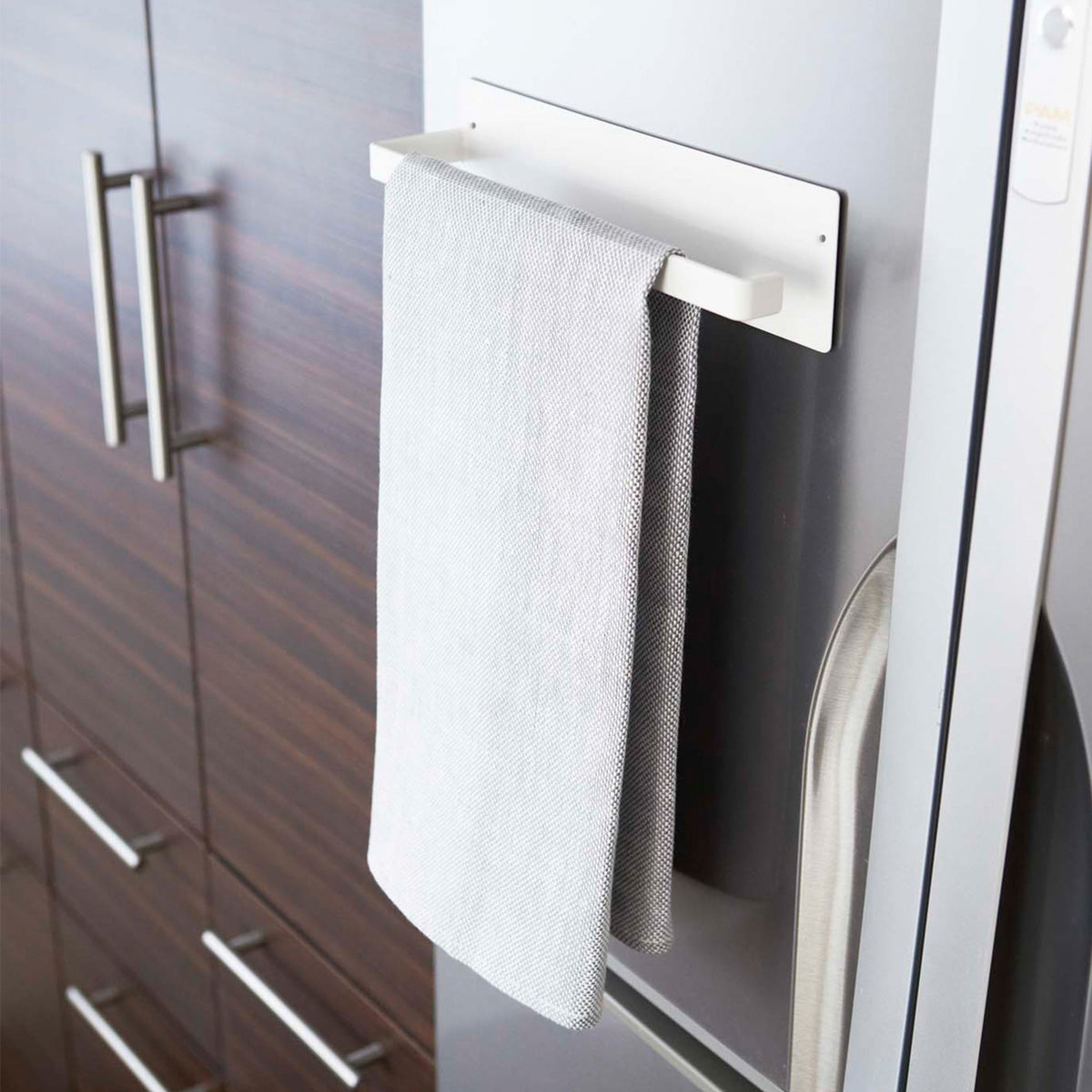 White Yamazaki Home Magnetic Paper Towel Holder - Steel on a refrigerator, used as a rail for light and dark grey kitchen towels hanging side by side.
