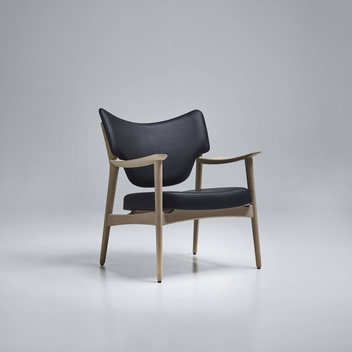Three-quarter view of the black Eikund Veng Lounge Chair in a gray studio, showing its open wood frame, extended sculpted armrests, and wing-shaped backrest.