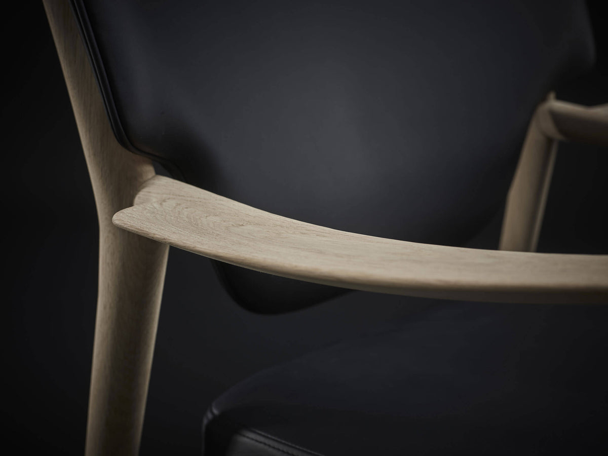 Close-up of the Eikund Veng Lounge Chair’s broad light wood armrest, showing visible grain and a gently scooped surface beside the black upholstered back.