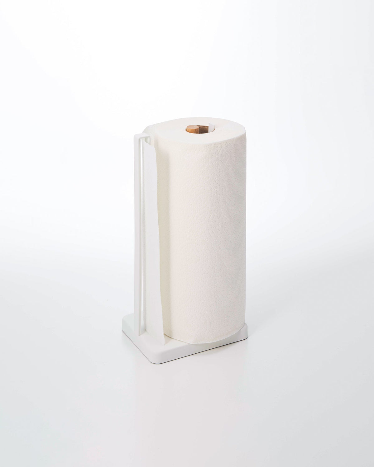 White Yamazaki Home Paper Towel Holder - Steel + Wood holding a paper towel roll on a pale background, with a rectangular base, tall side rail and wooden centre post visible through the roll.