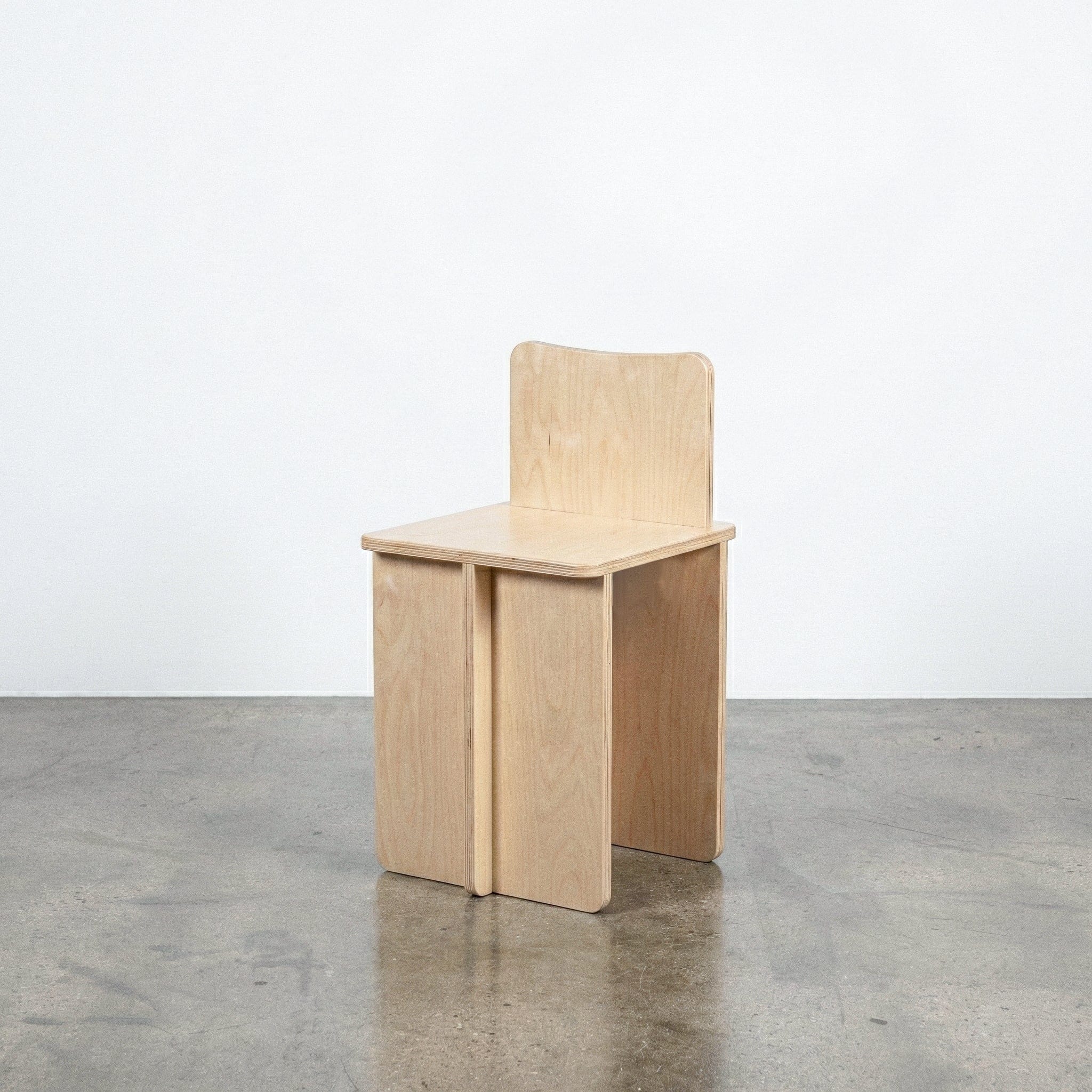 Studio Furnis Williamsburg natural wood chair with a gently curved backrest, flat square seat and broad panel legs on a polished concrete floor