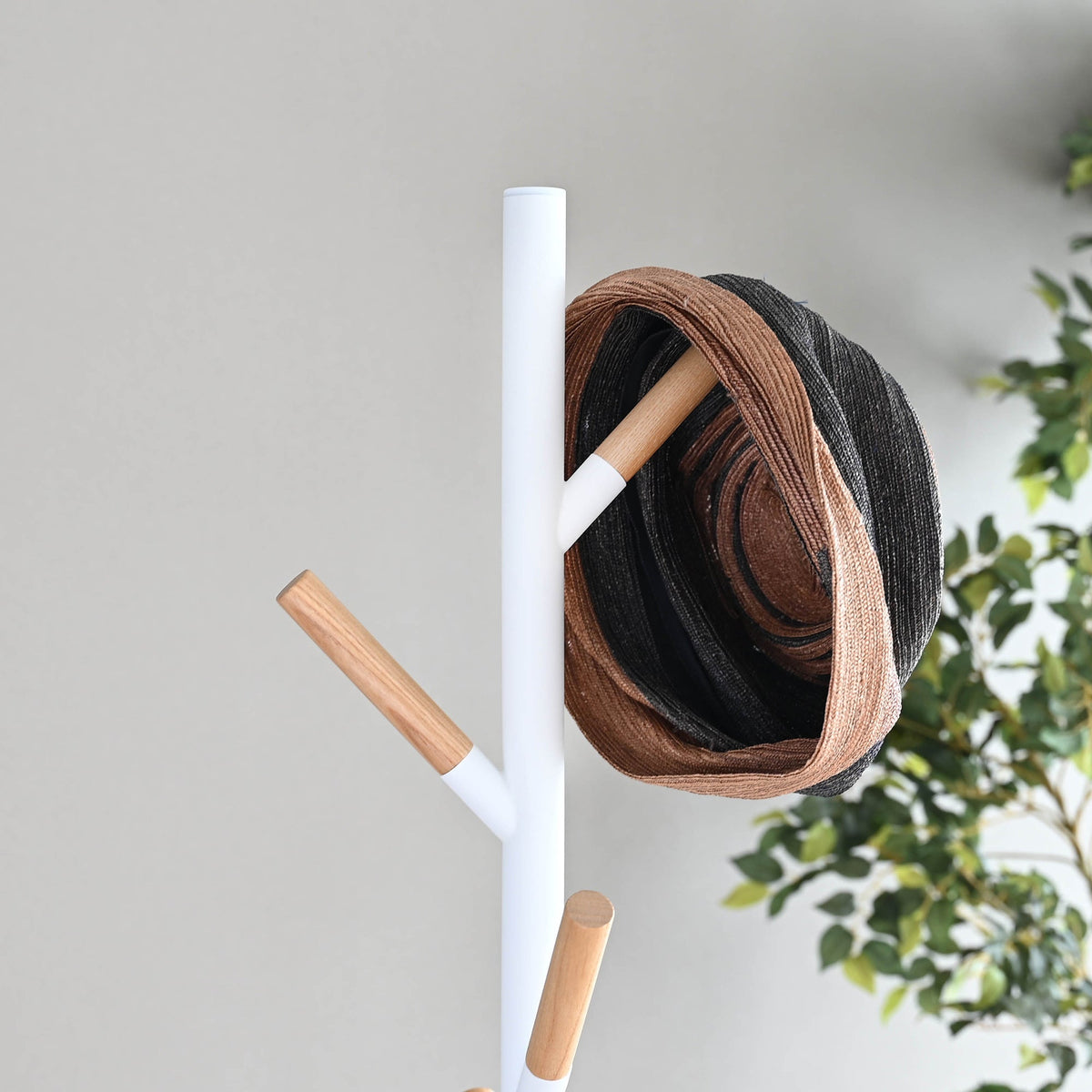 Close-up of the white Yamazaki Home Coat Rack (70" H) - Steel upper branches, showing light wood tips and layered brown and dark hats hanging beside the pole.