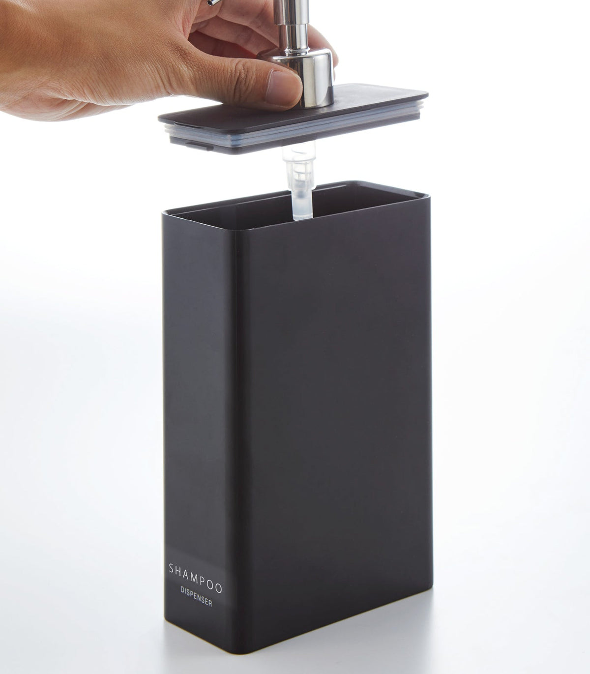 A hand lifts the silver pump and flat lid from the black Yamazaki Home Rectangle Shower Dispenser - Three Styles, revealing its wide rectangular opening and clear intake tube.