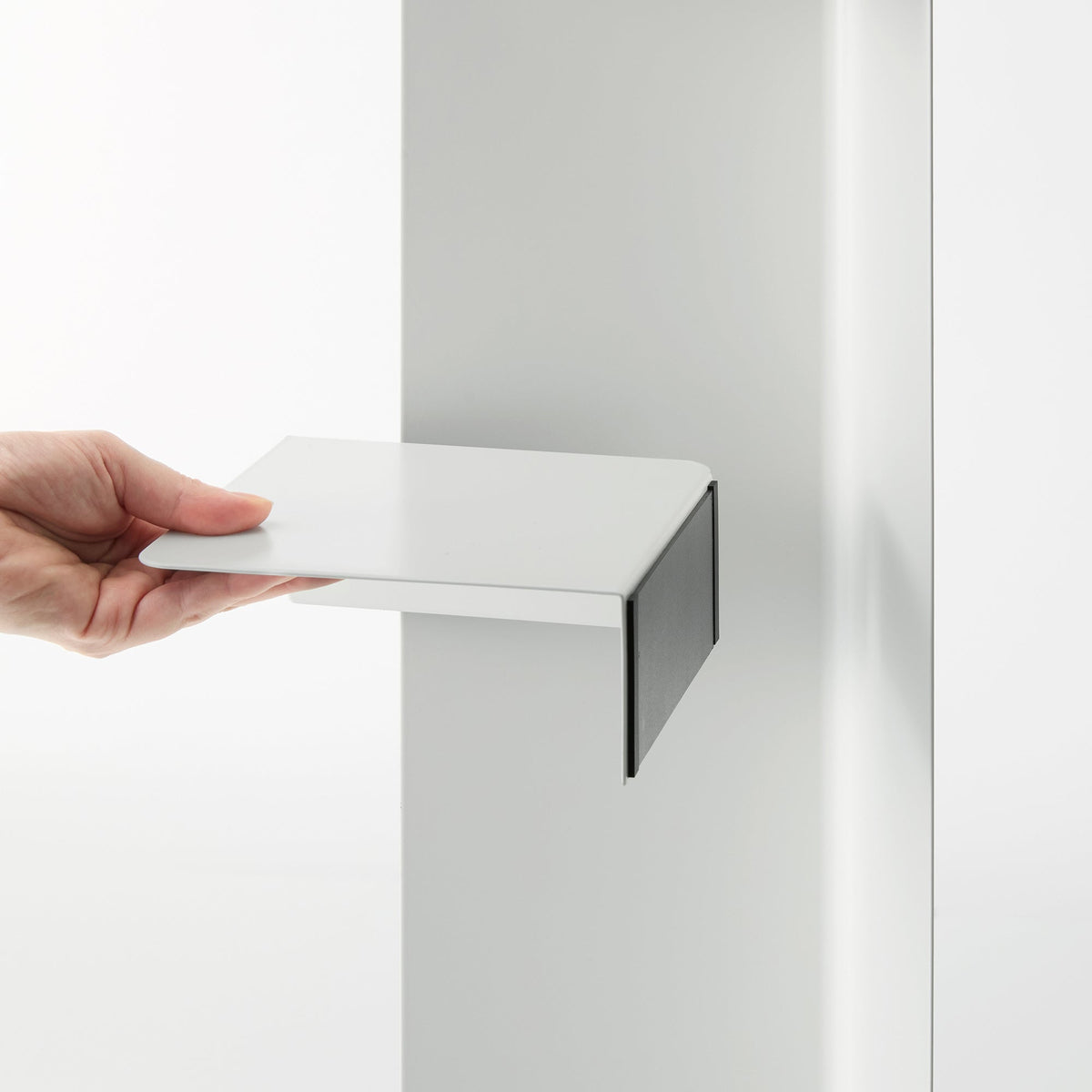 Close-up of a hand holding the white shelf component of the Yamazaki Home Rolling Bathroom Organizer - Steel away from its vertical panel, showing the flat surface and downward-bent side.