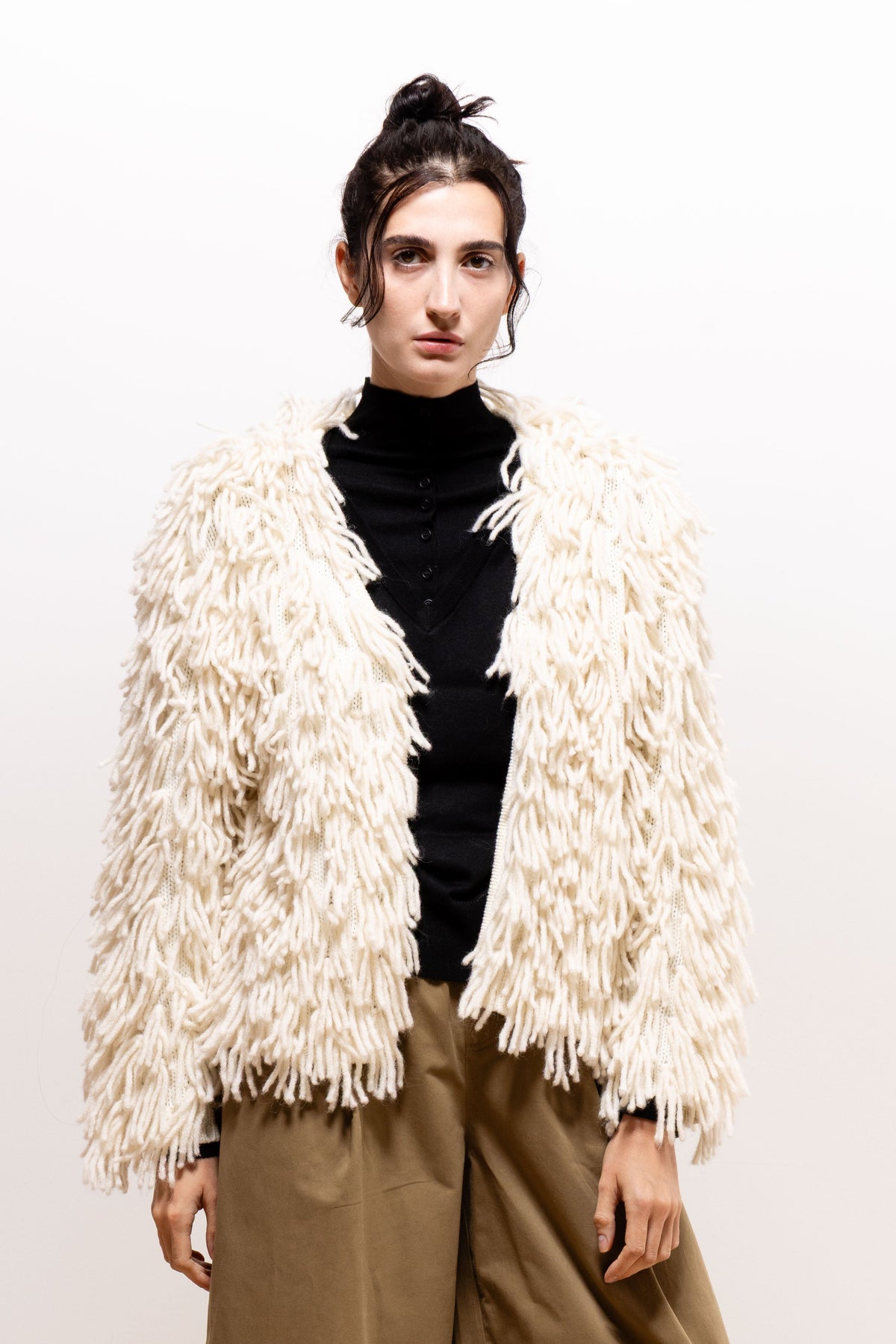 Model wearing the ivory Paulette Saint-Jean-de-Luz Cardigan open over a black high-neck top and khaki-brown trousers, showing the shaggy front edges and long sleeves.