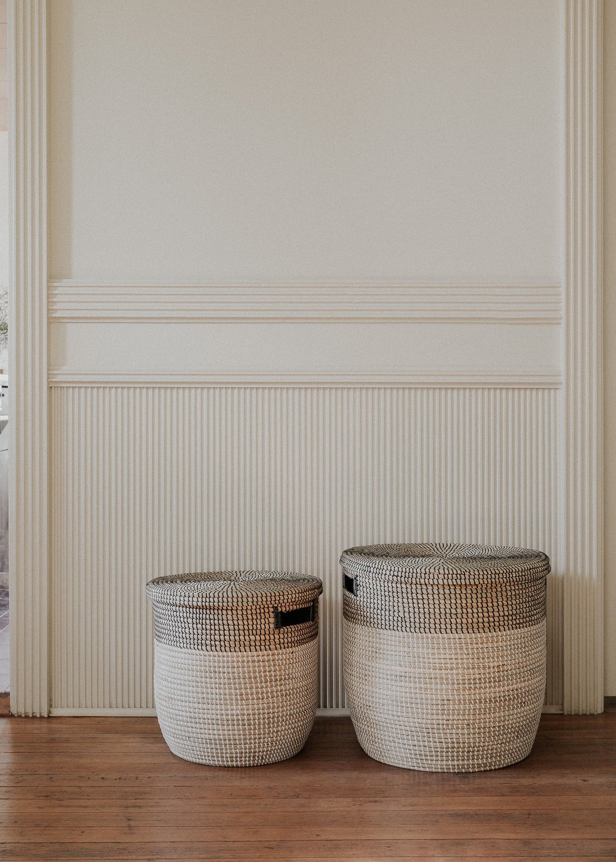 Two Black Medina baskets arranged beneath decorative wall molding in a minimal interior.